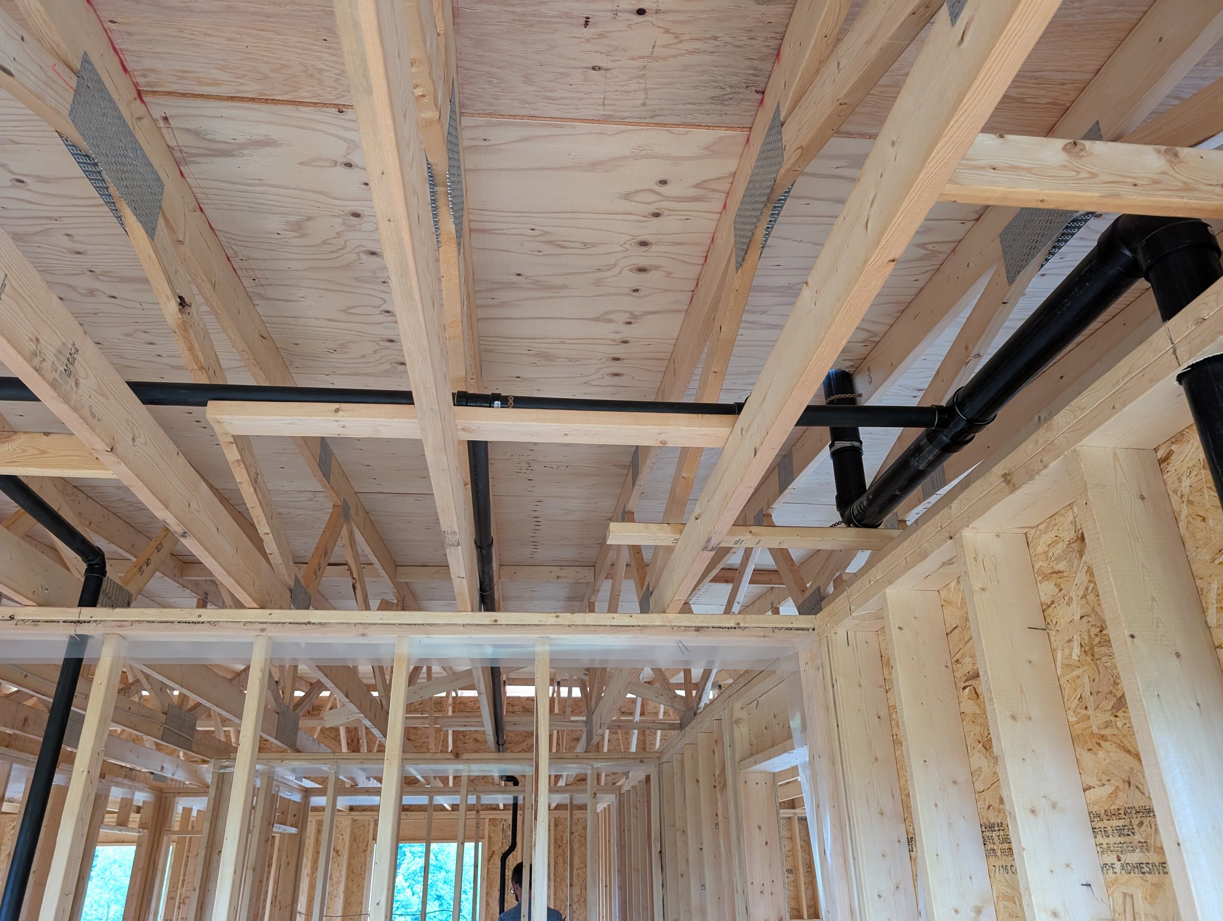 Interior view of a building under construction, showing wooden framing and black plumbing pipes.