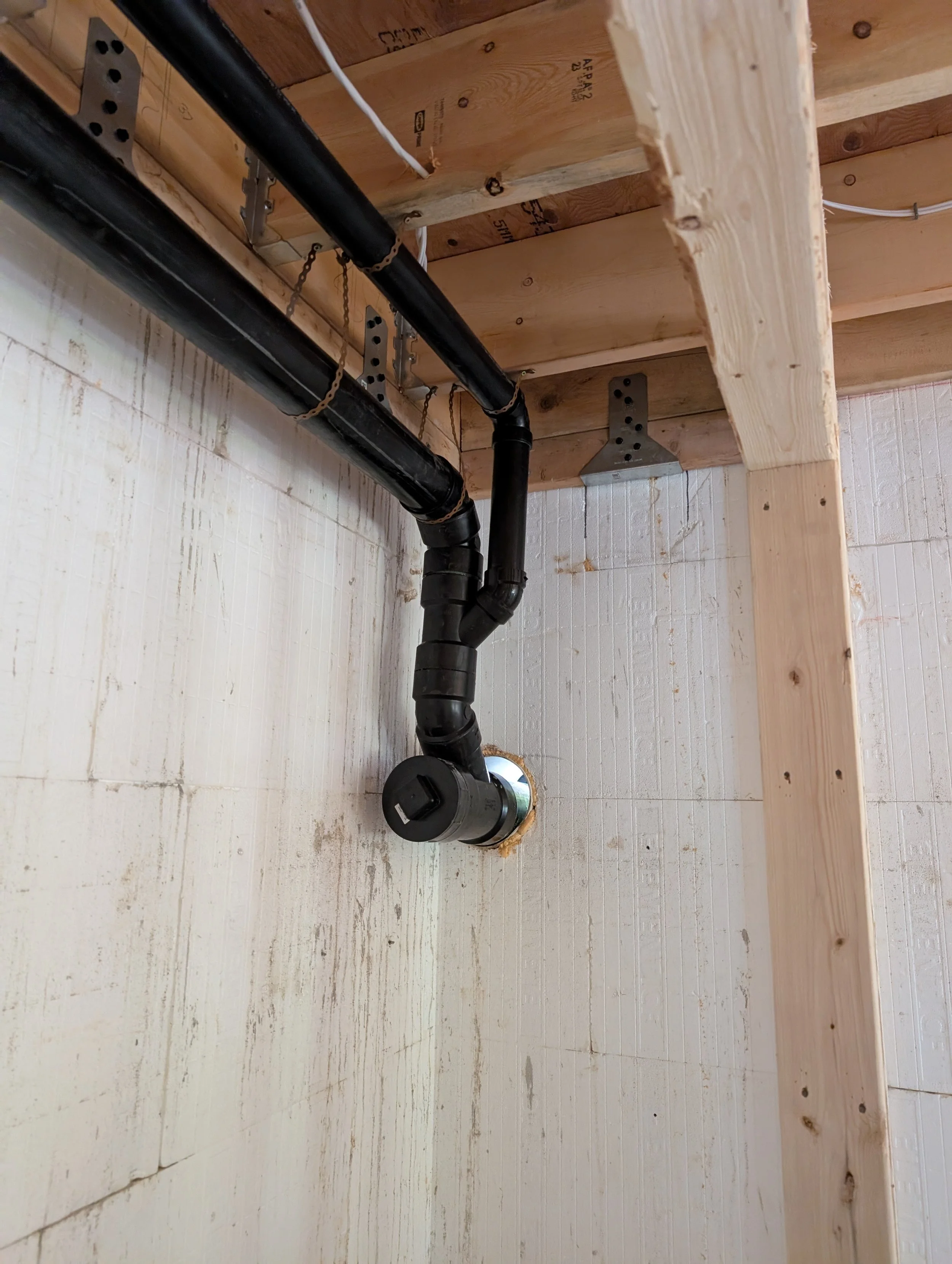 Interior view of a wooden ceiling with black pipes and a black electrical device on the wall, with drywall and some exposed wall studs.