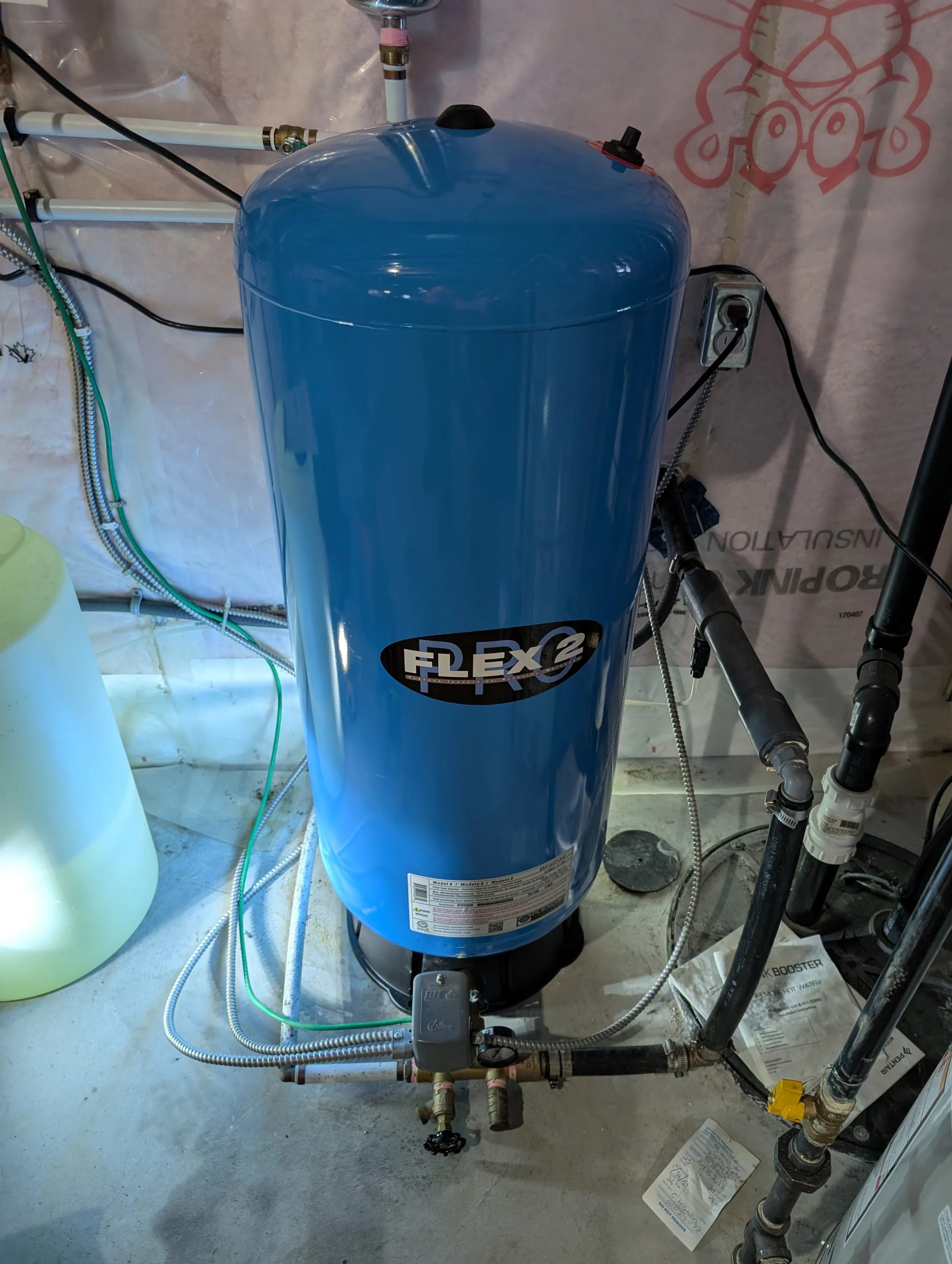 A blue Flex condensate pump connected to plumbing and electrical wiring in a utility or mechanical room. The pump is situated on the concrete floor with pipes and wires attached.