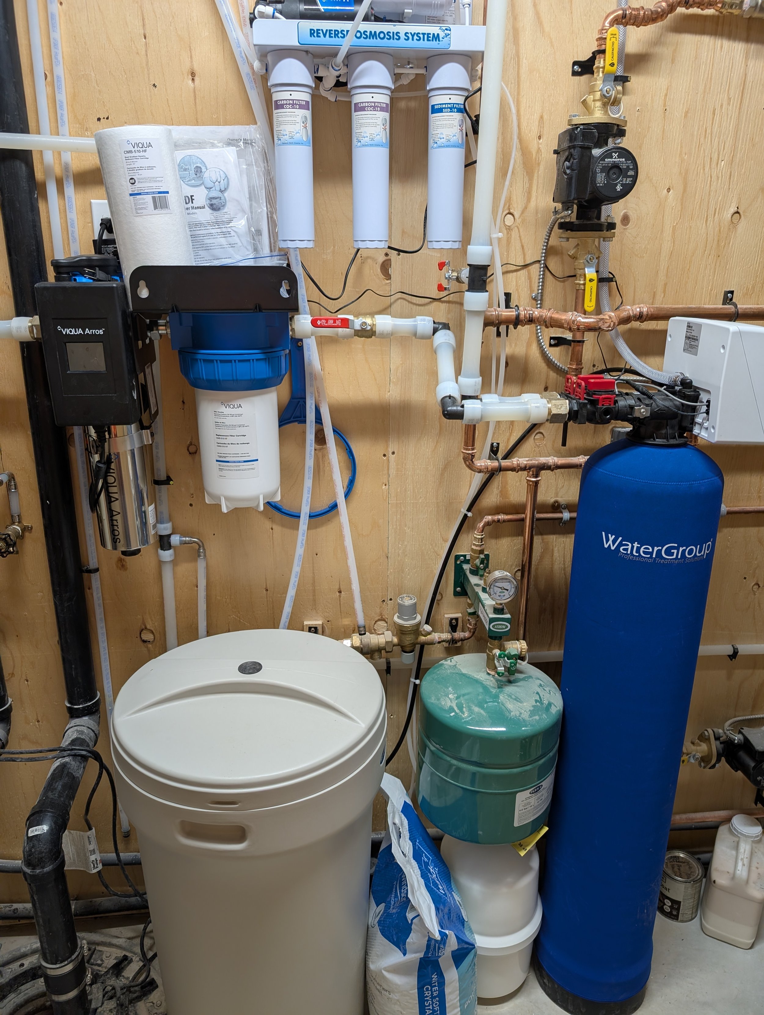 A reverse osmosis water filtration system installed on a wooden wall, with various filters, tanks, and plumbing components.