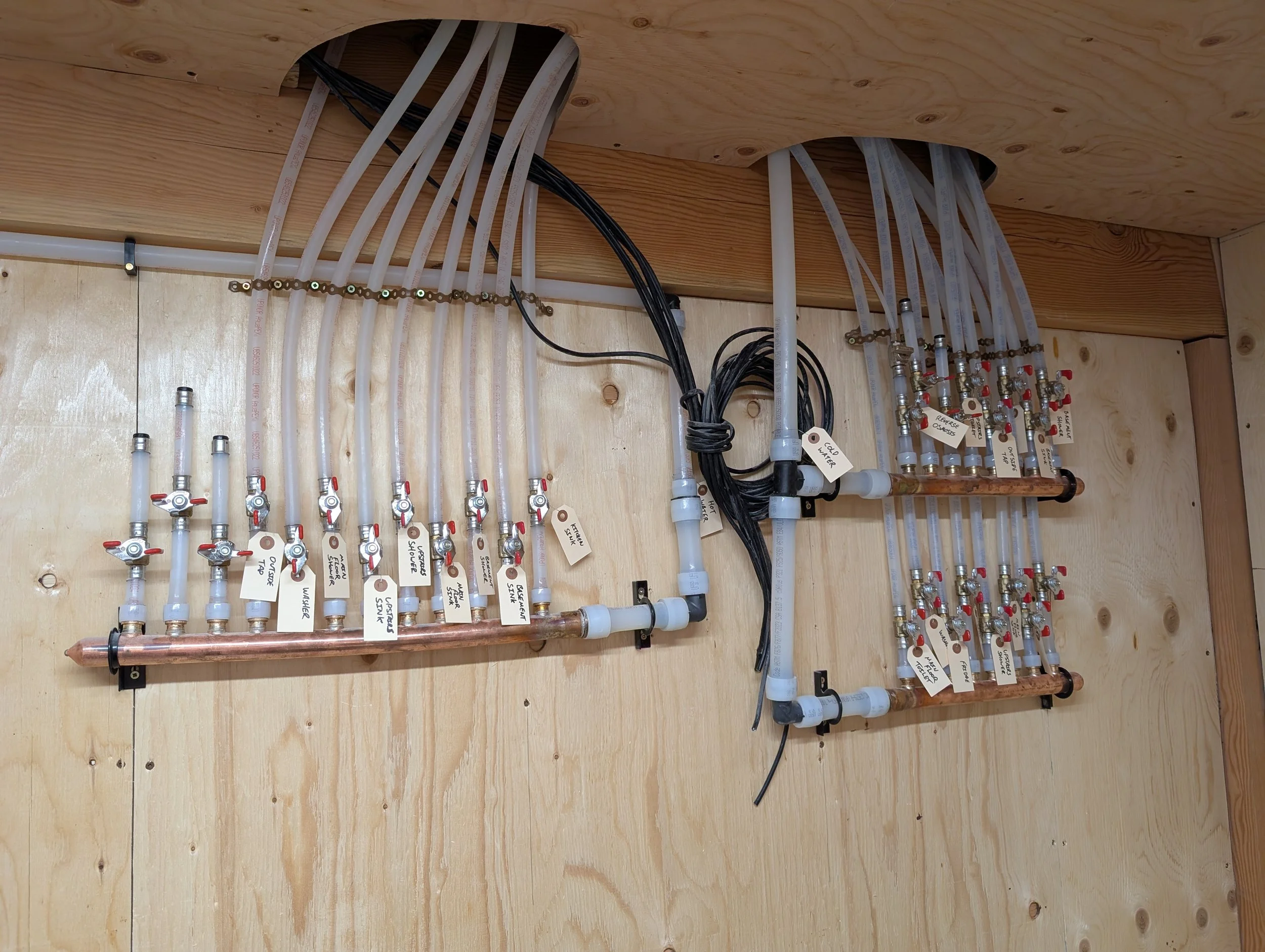 A plumbing and piping system with various white plastic pipes, valves with red handles, and labels for different connections mounted on a wooden wall or panel.