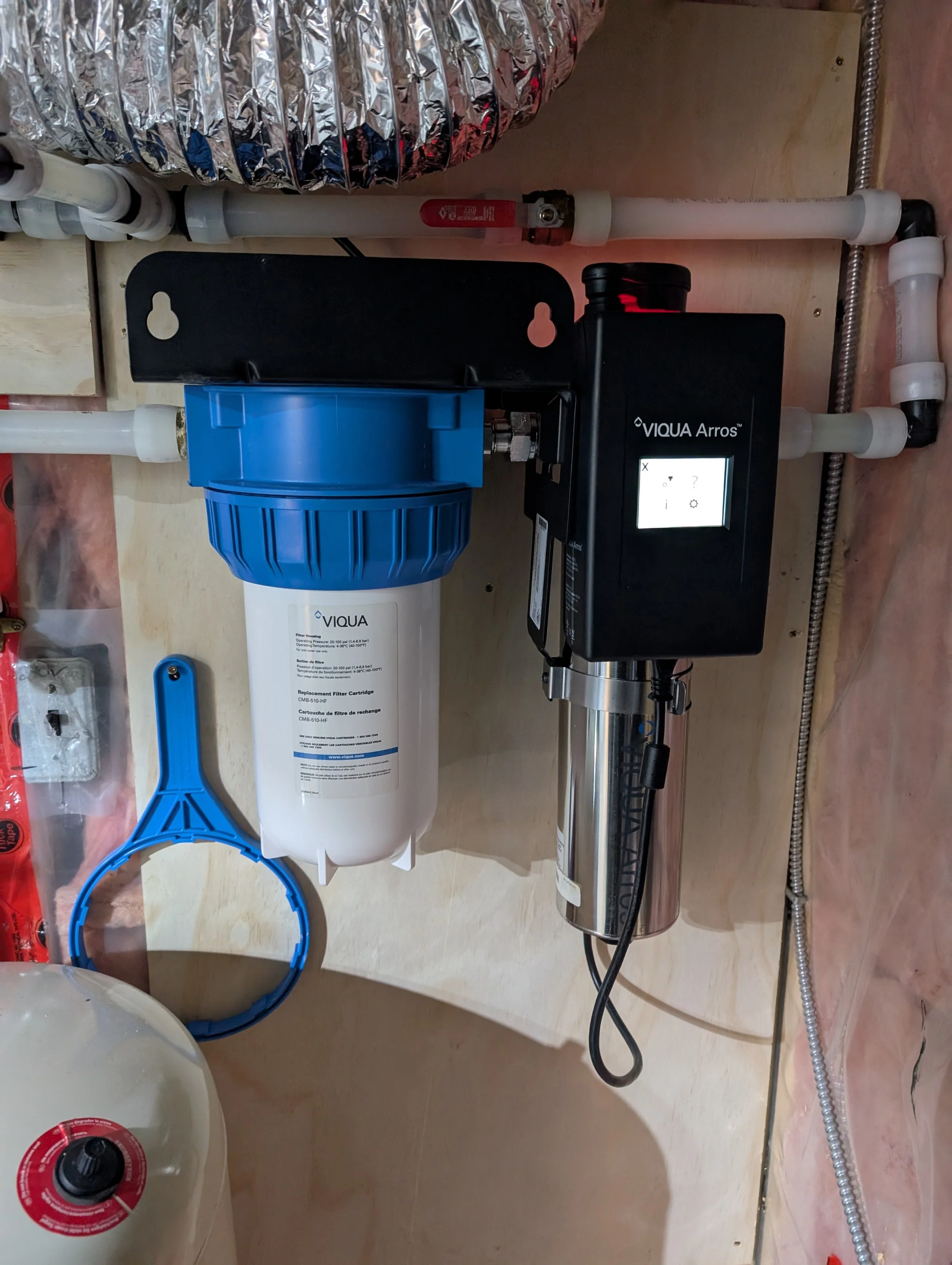 A water filtration system installed on a wall, including a filter cartridge and related piping and components.