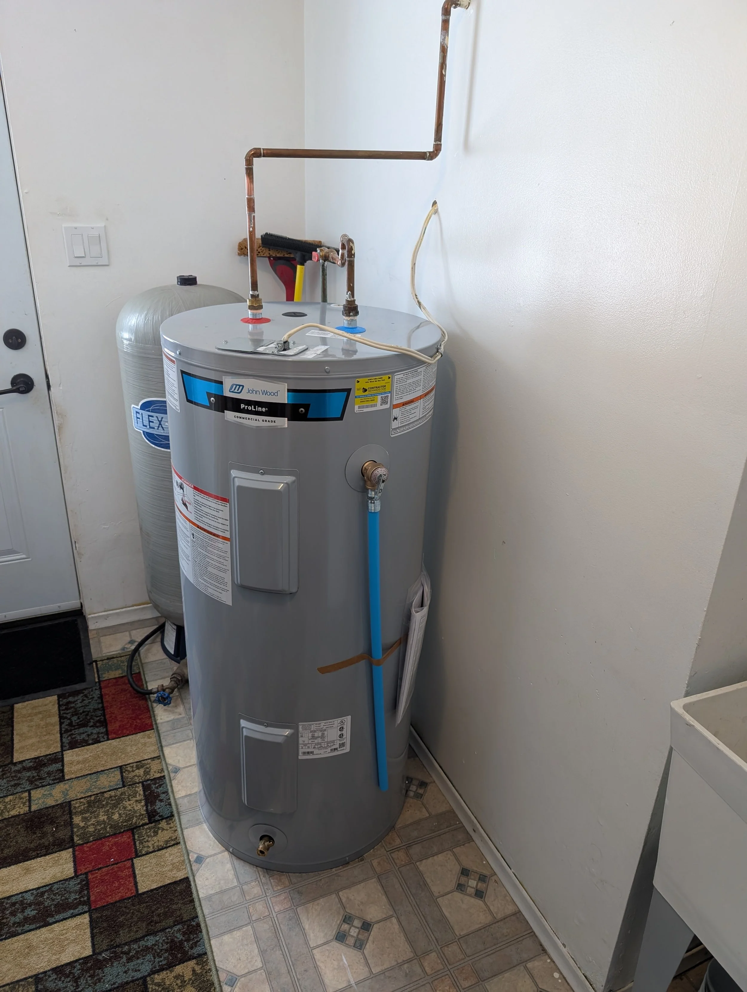 A water heater with copper piping and black, red, blue, and yellow shutoff valves in a utility room, next to a water filter system and a closed door.