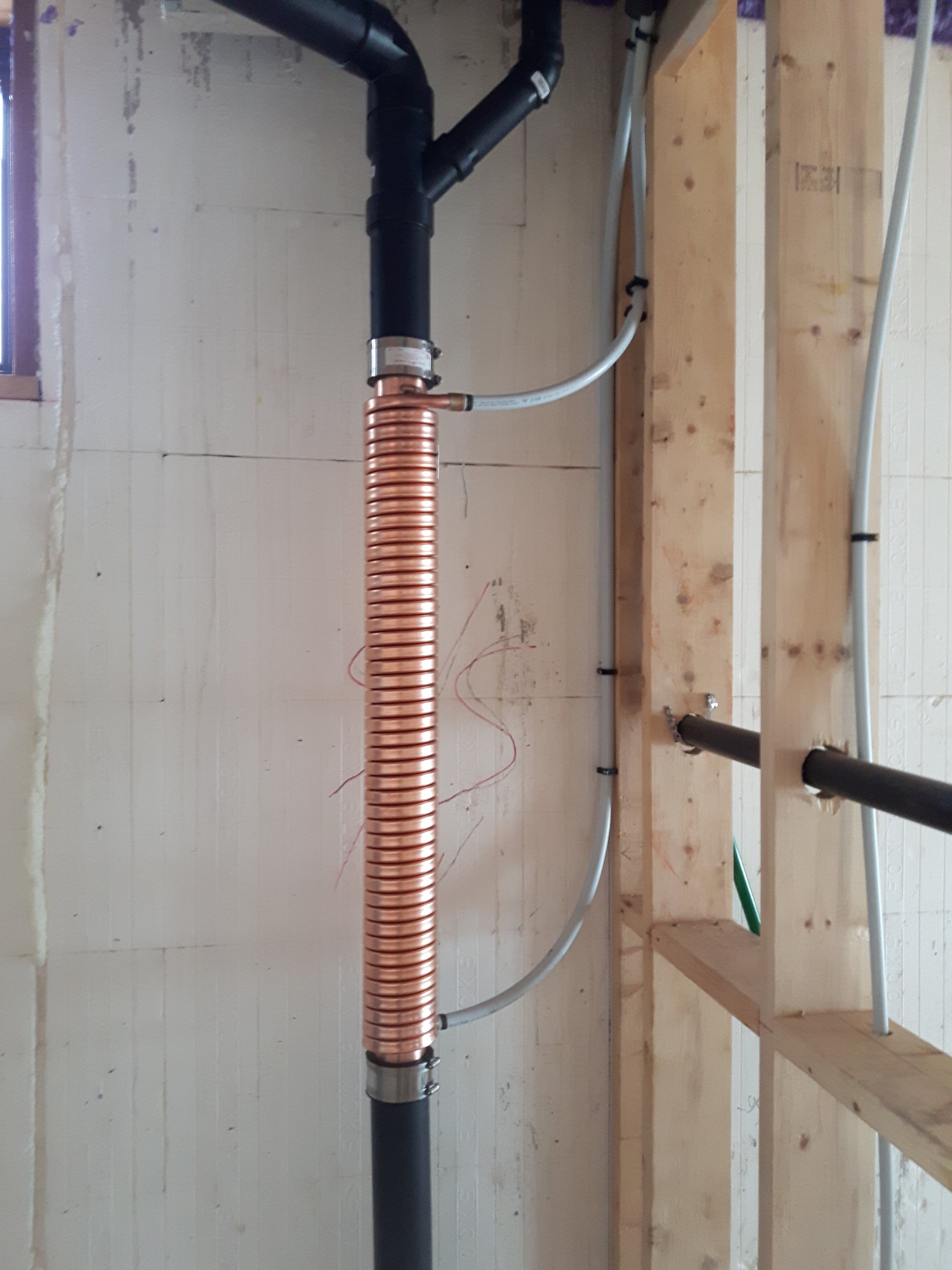 Plumbing pipes including black PVC, copper, and gray flexible tubing installed in an unfinished wall.