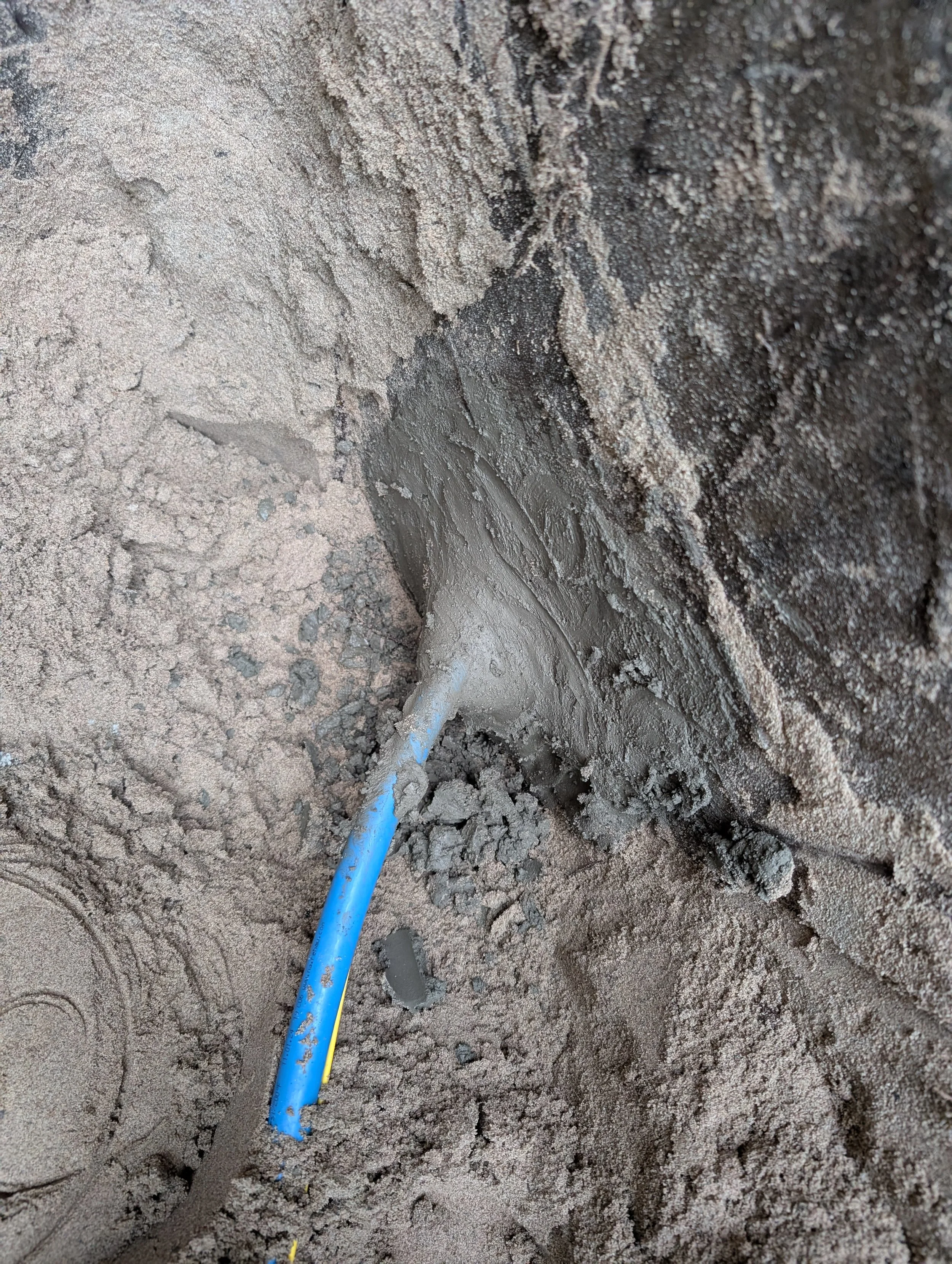 A close-up photograph of a blue electrical cable underground in brown soil. The cable appears to be in the process of installation or repair.
