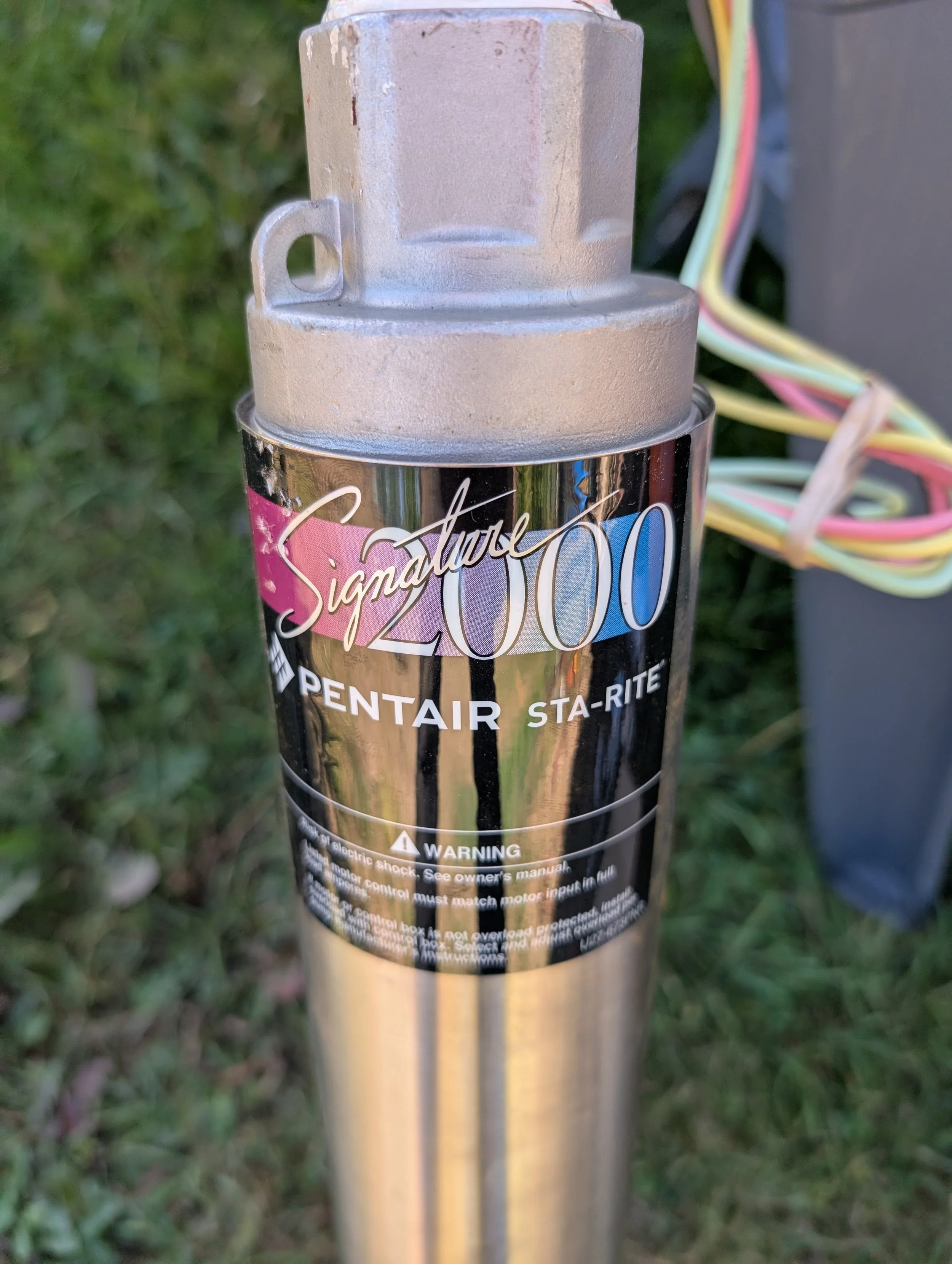 Close-up of a cylinder with a label that reads "Sigma 2000" attached to a metal pole, with wires connected to the pole, against a background of grass.
