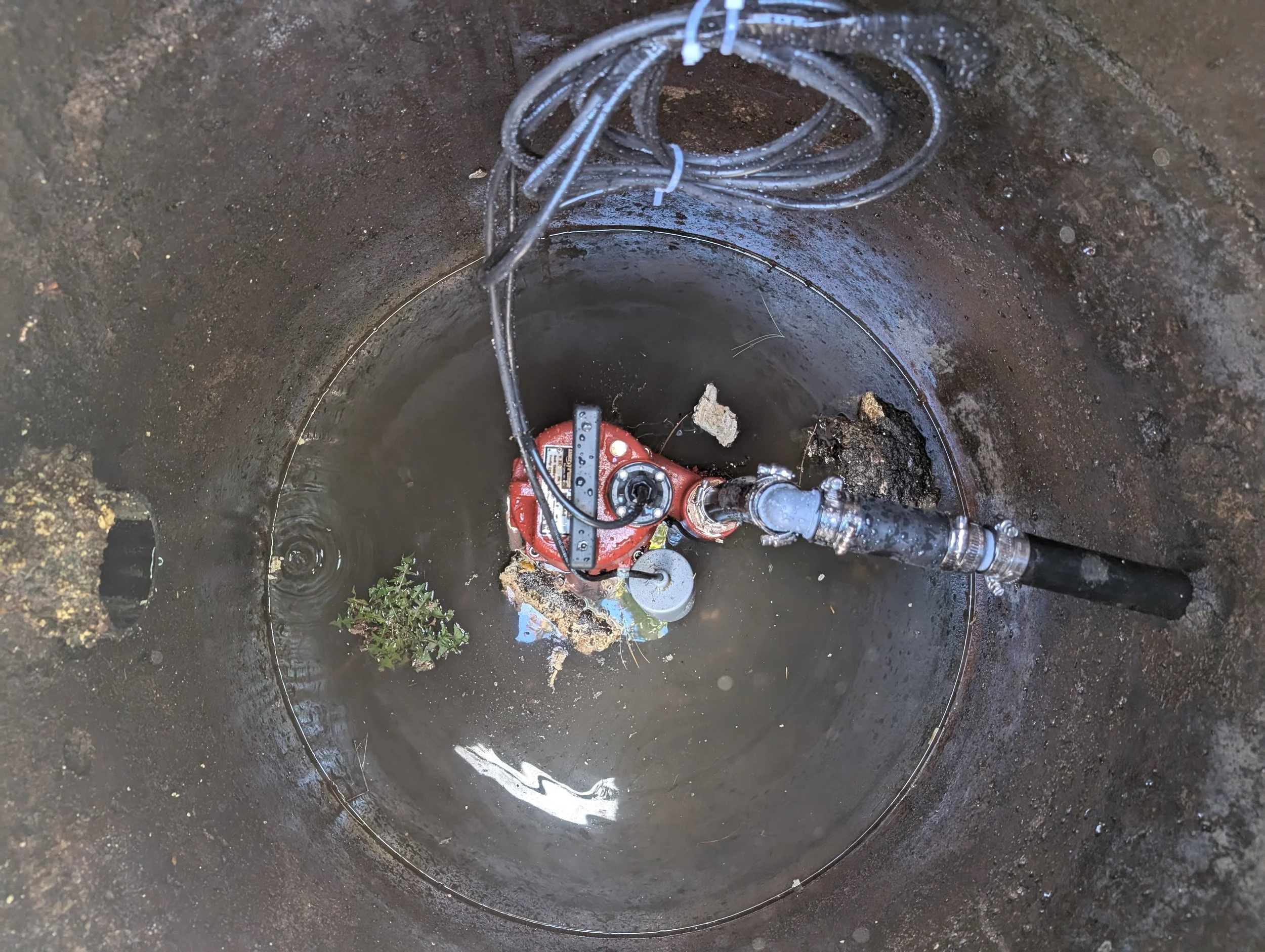 Inside a sewer or pipe with a red pump and electrical wires, with wet, dark walls.