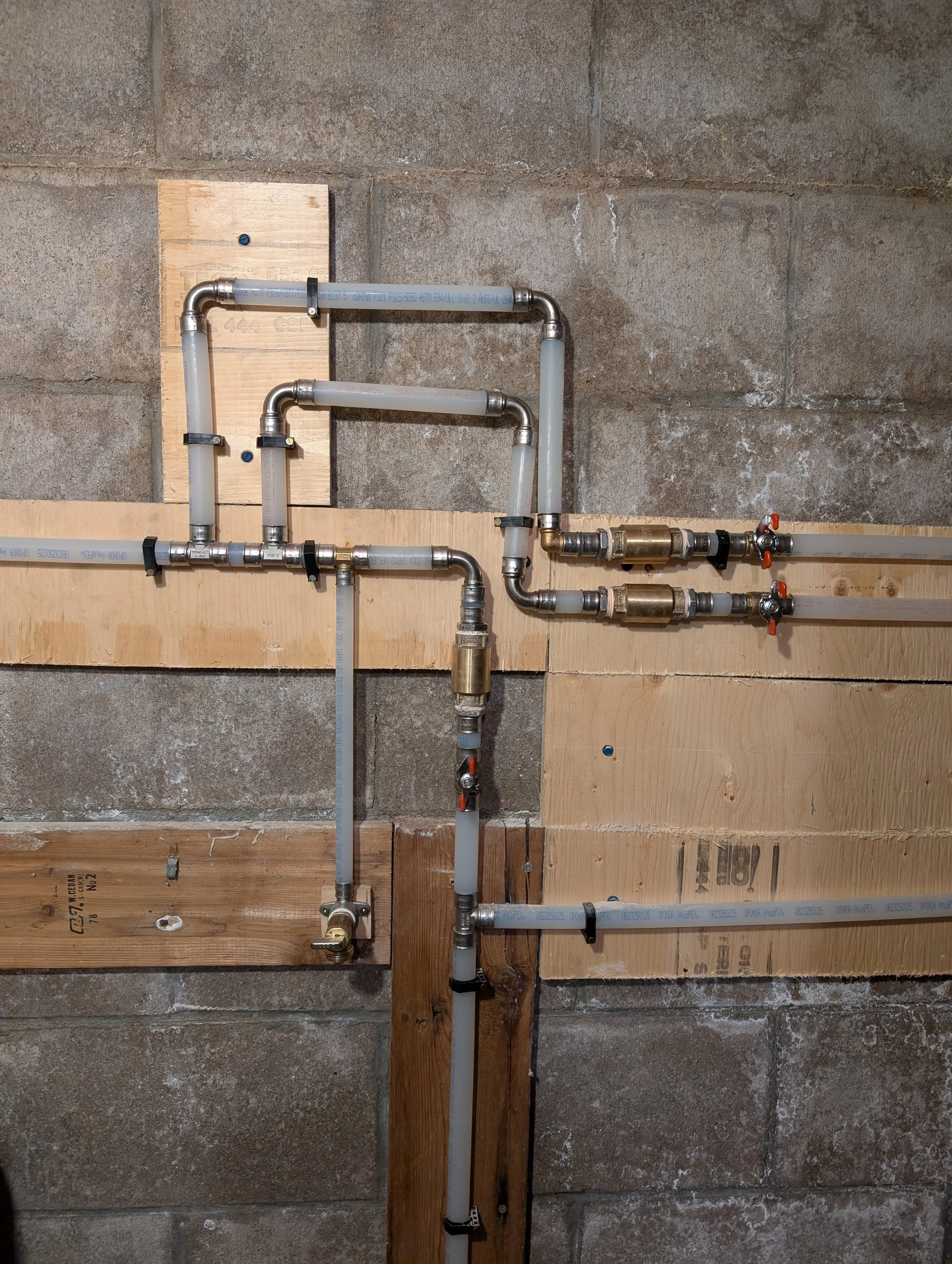 A plumbing system installed on a concrete wall, consisting of PVC pipes, elbows, valves, and fittings fixed to wooden boards.