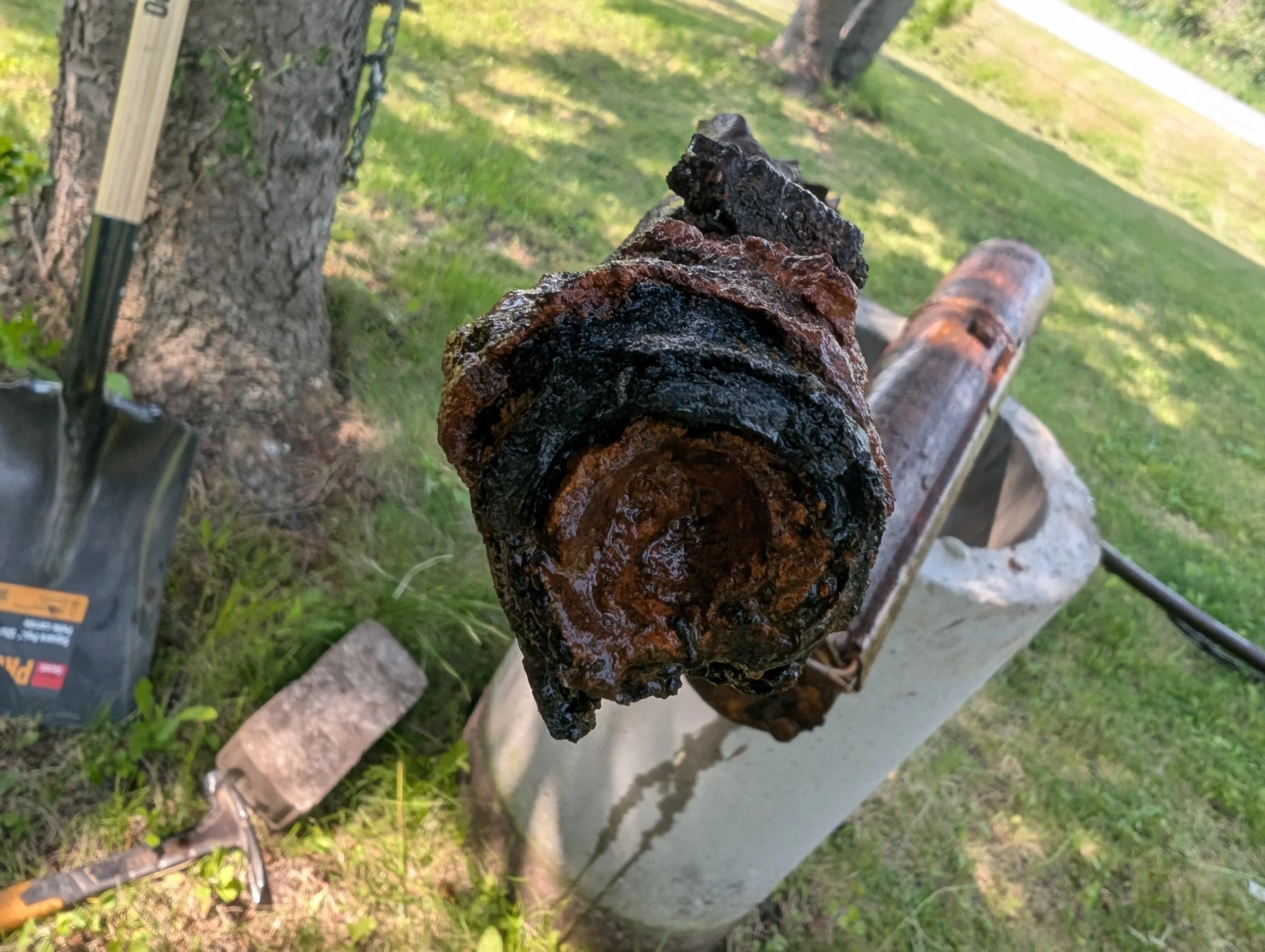 Close-up of a rusty, charred piece of metal on a metal surface with green grass and trees in the background.