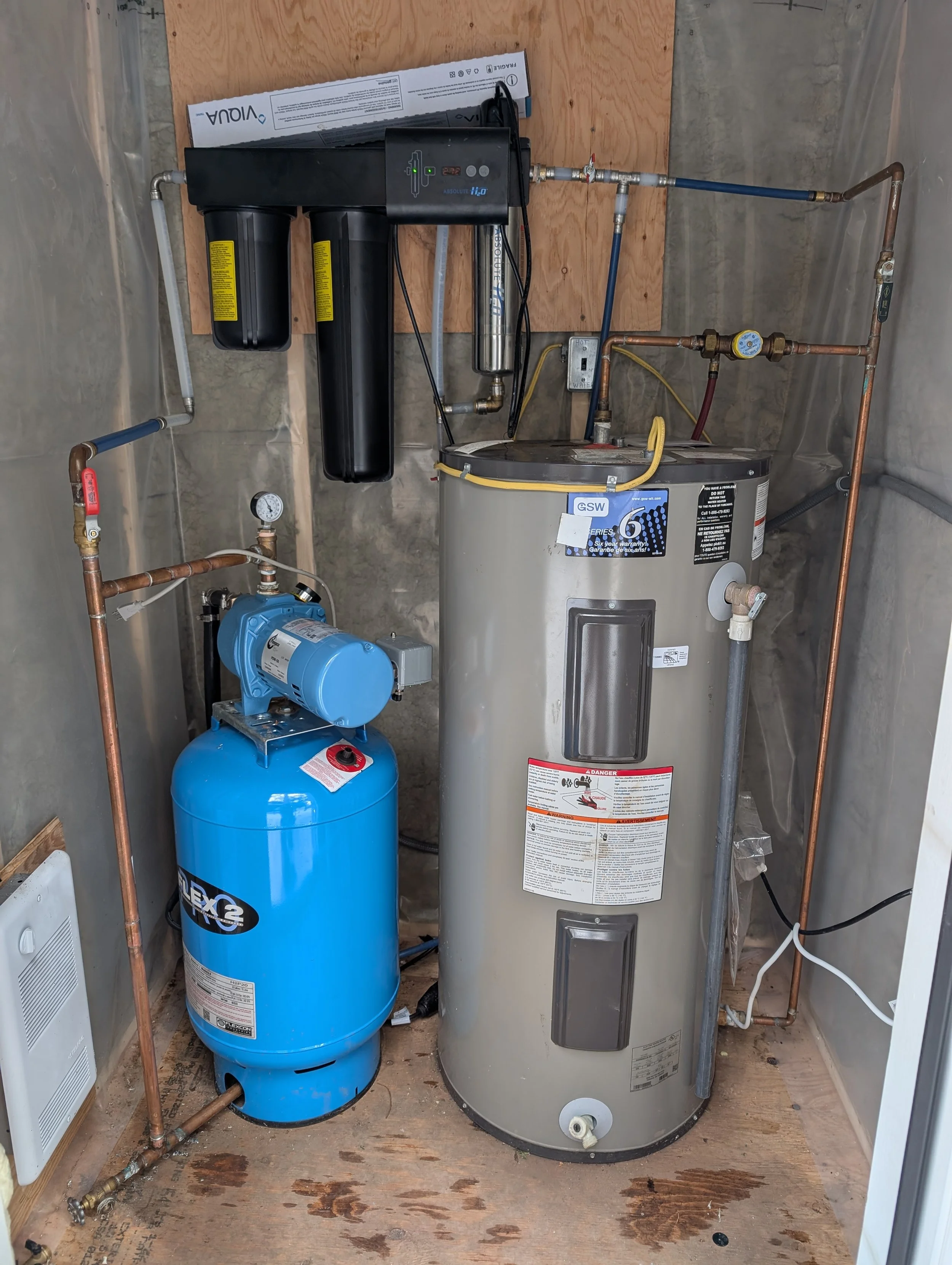 A water treatment system with a blue pressure tank, a gray water heater, and various pipes and connections in a utility room