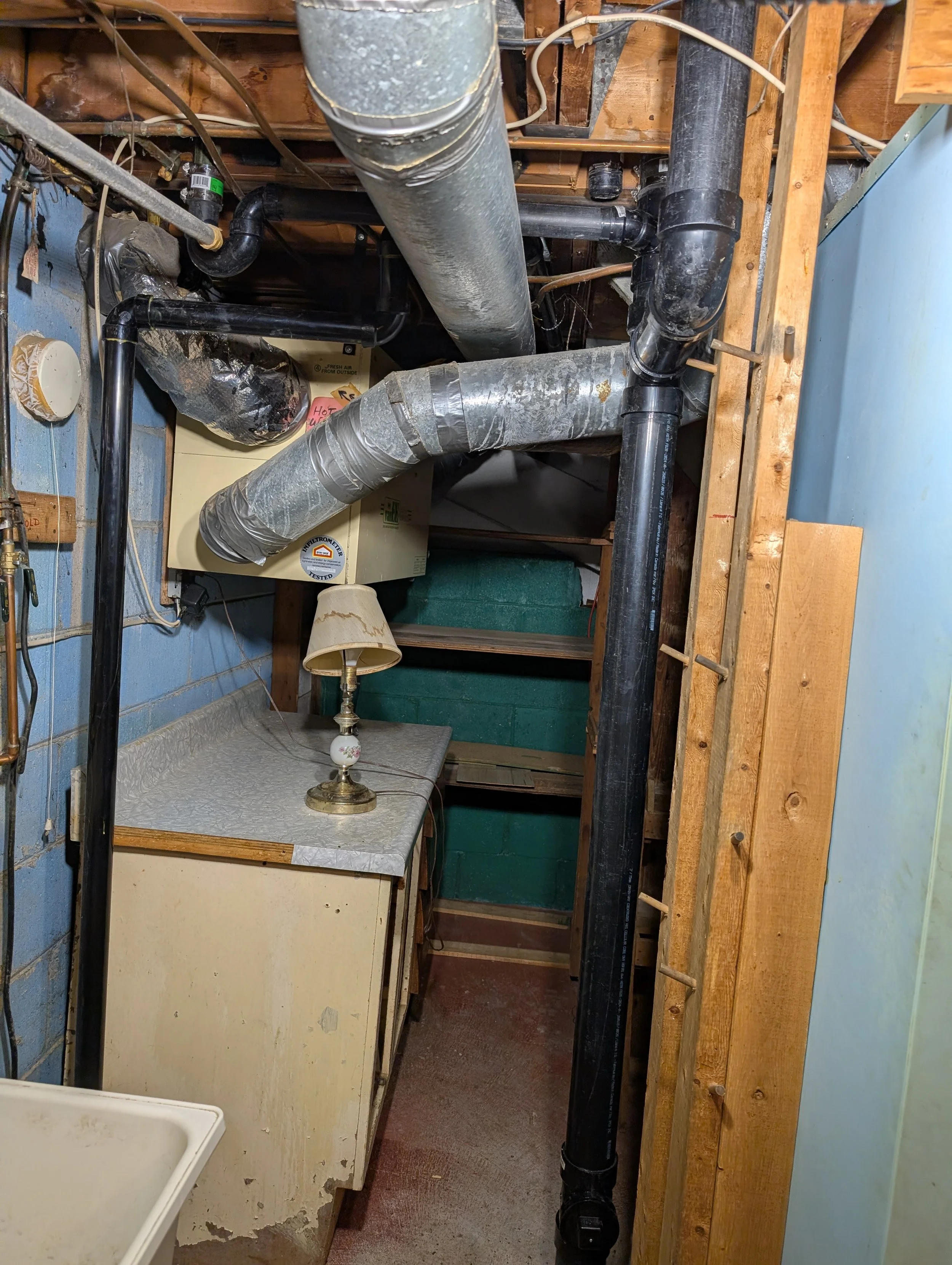 View of a basement with exposed wooden beams, black plastic pipes, a furnace, a small lamp, and laundry area.