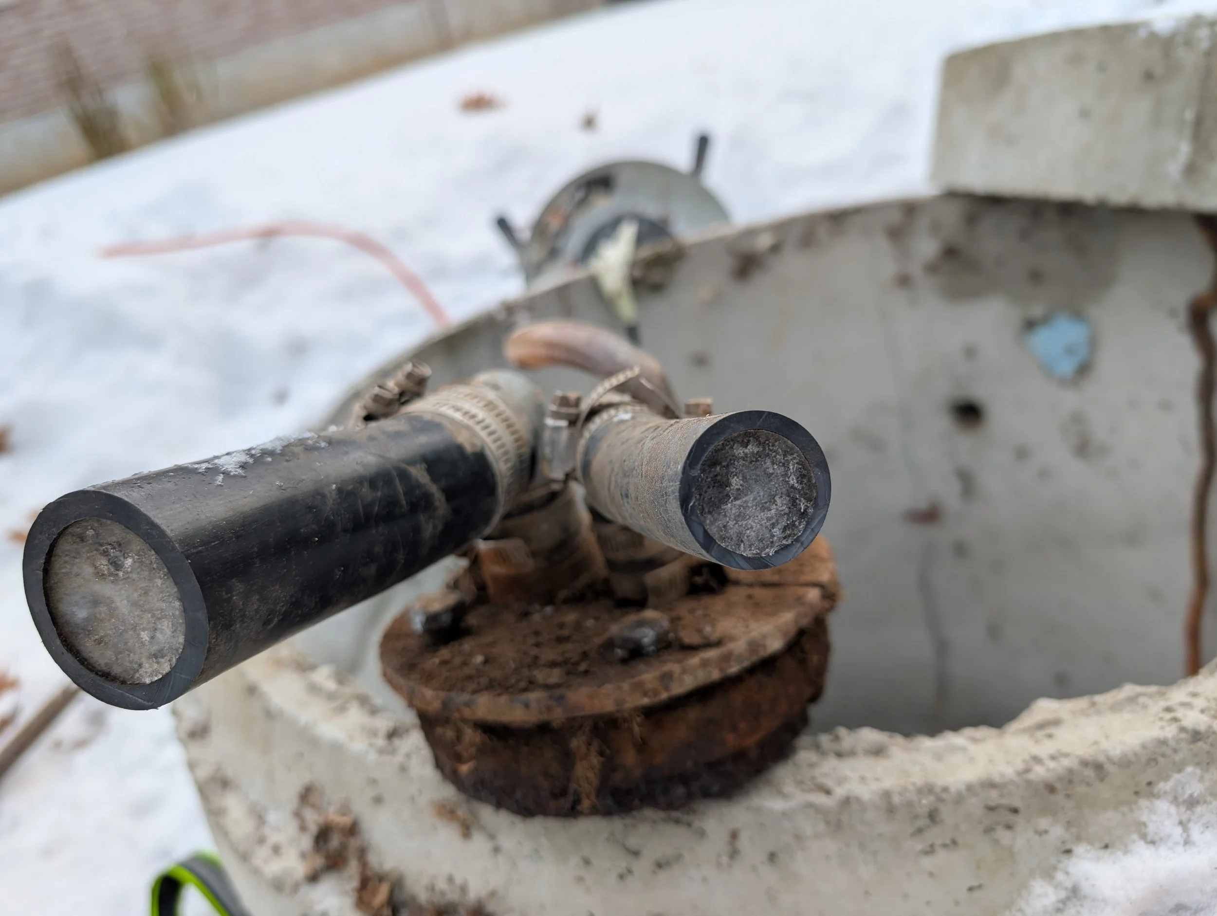 A close-up view of a rifle scope mounted on a rifle, positioned on a rusty metal surface outdoors, with snow and a brick wall in the background.