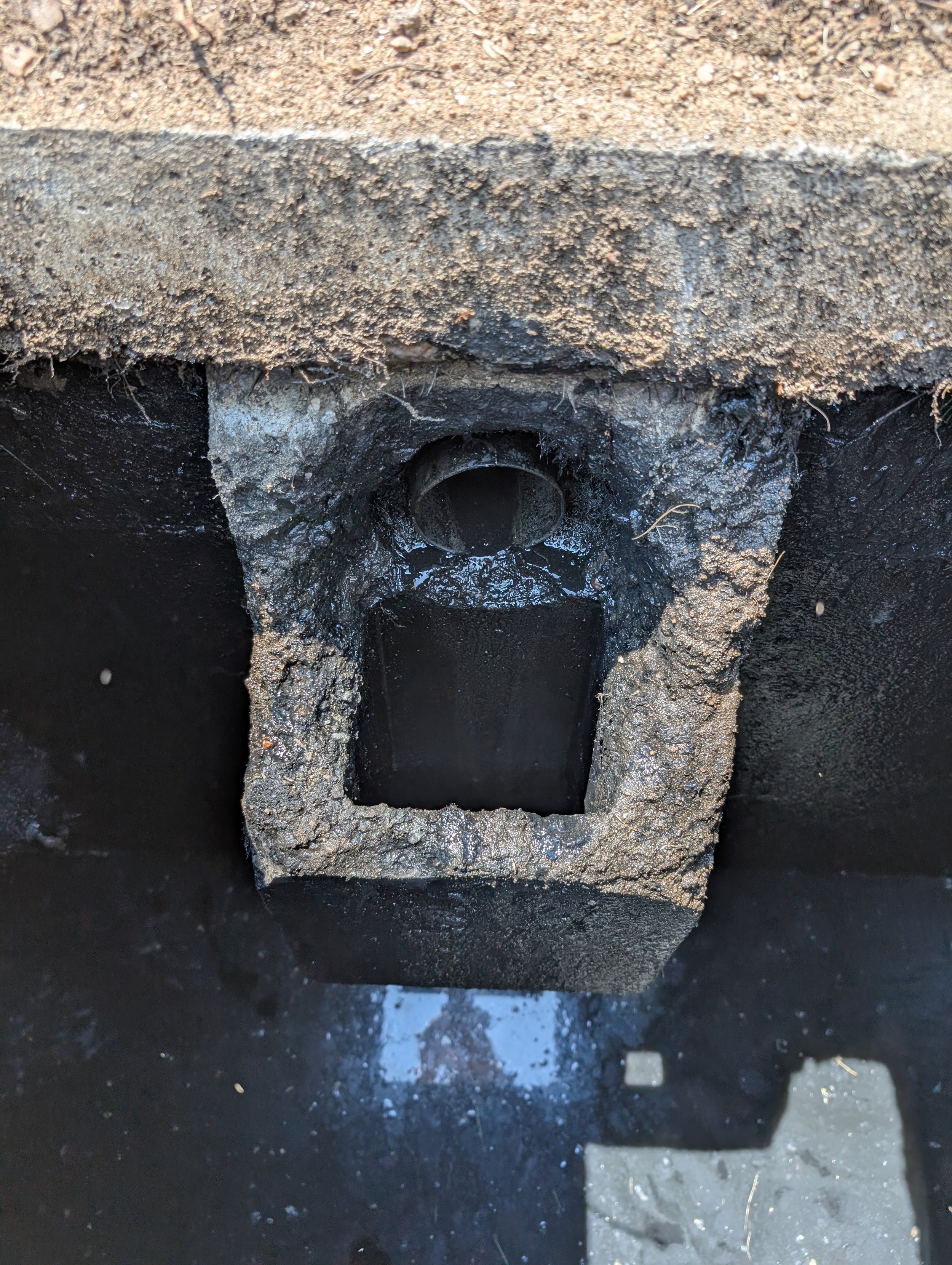 Close-up of a drain pipe embedded in soil and asphalt, with surrounding dirt and gravel.