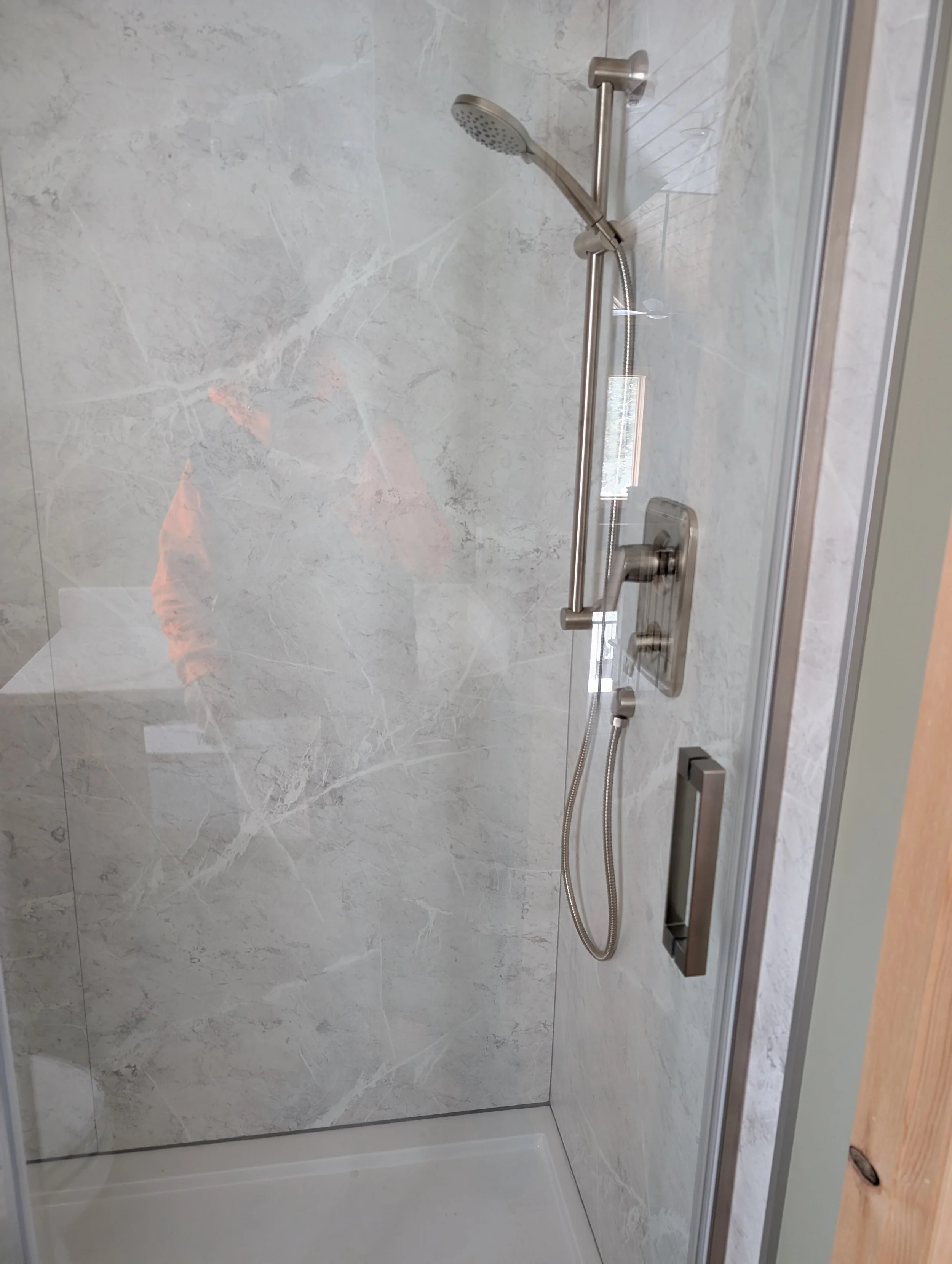 Shower with gray marble walls, a handheld shower head, a rectangular shower control panel, and a glass door.