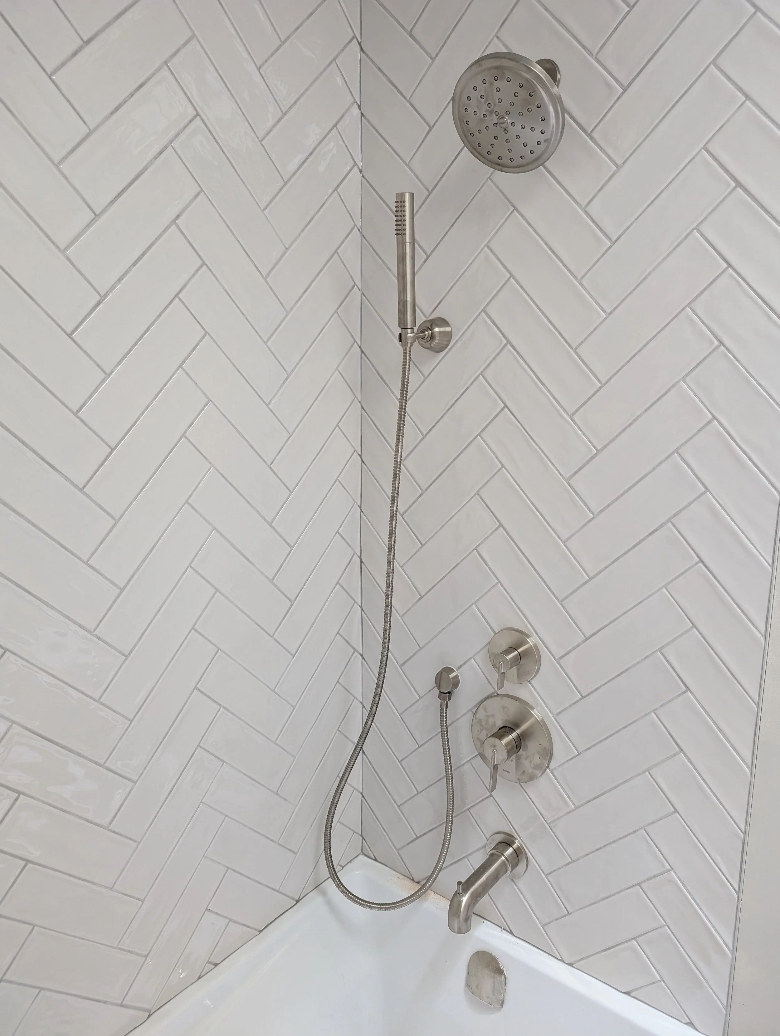 Shower with white subway tile walls, a round showerhead, a handheld shower wand, and three control knobs.