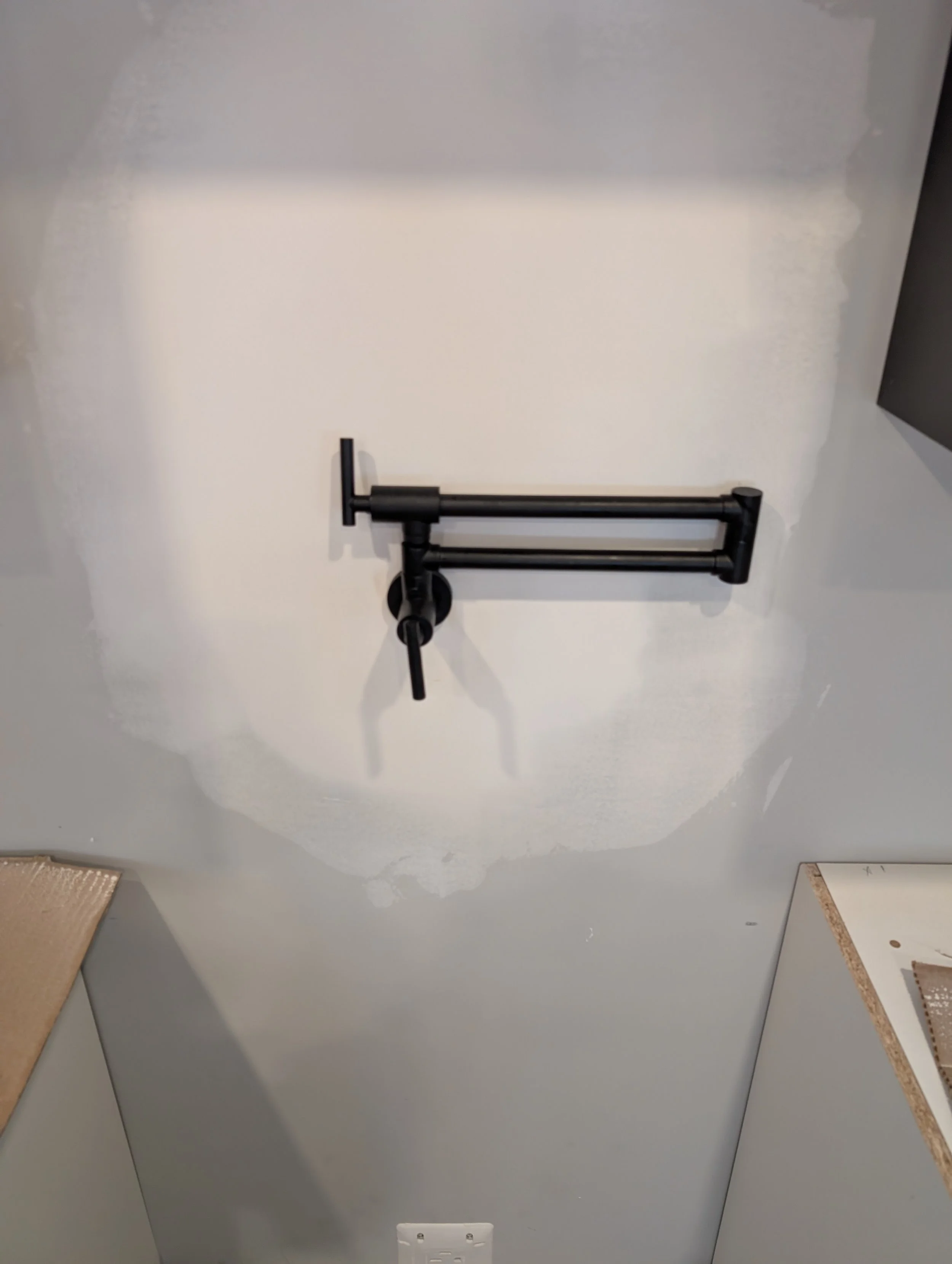 A black hand truck with a folding handle is mounted on a white wall.