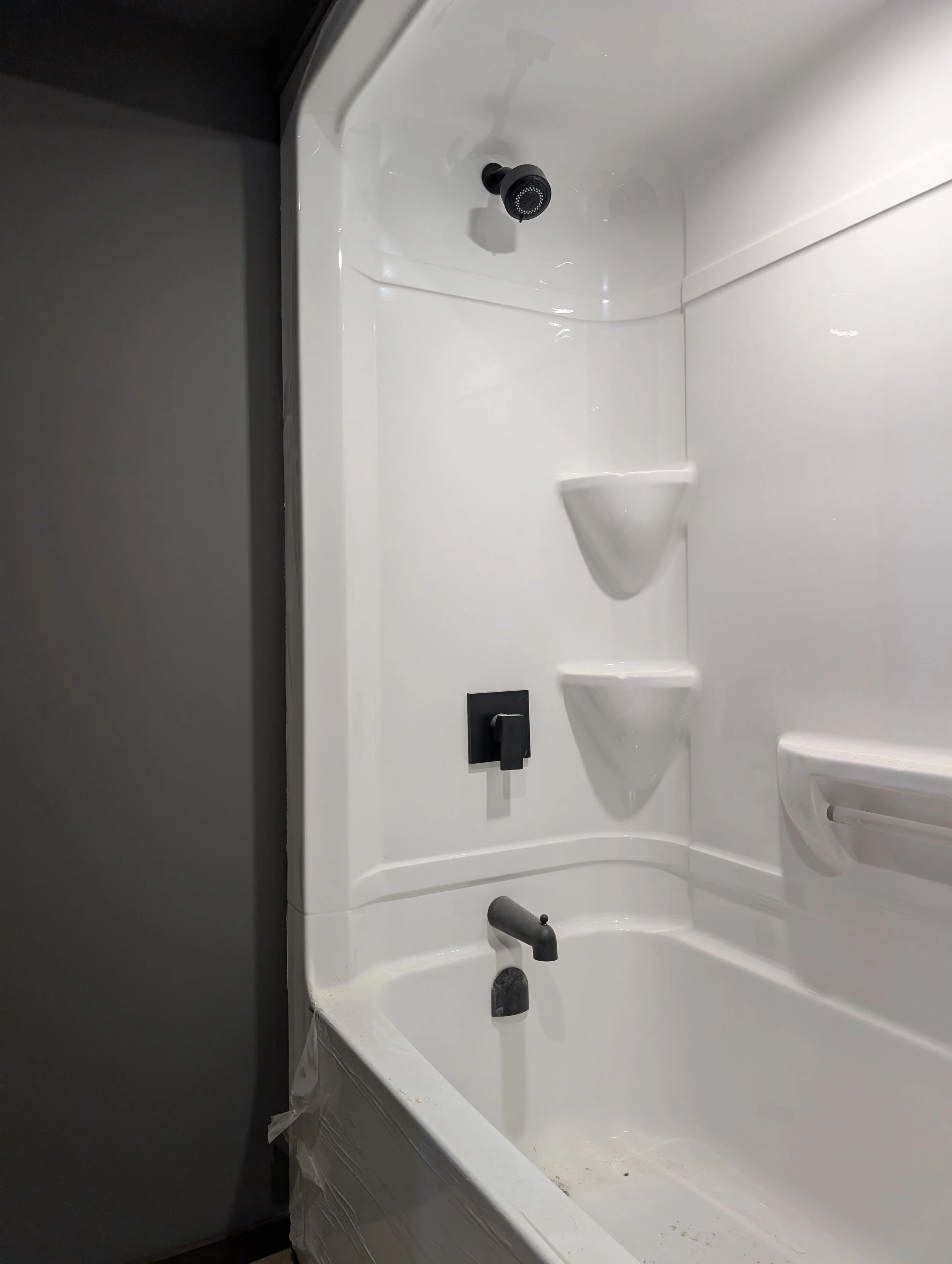 Empty shower with a black shower head, black faucet, built-in soap holder, and curved white walls.