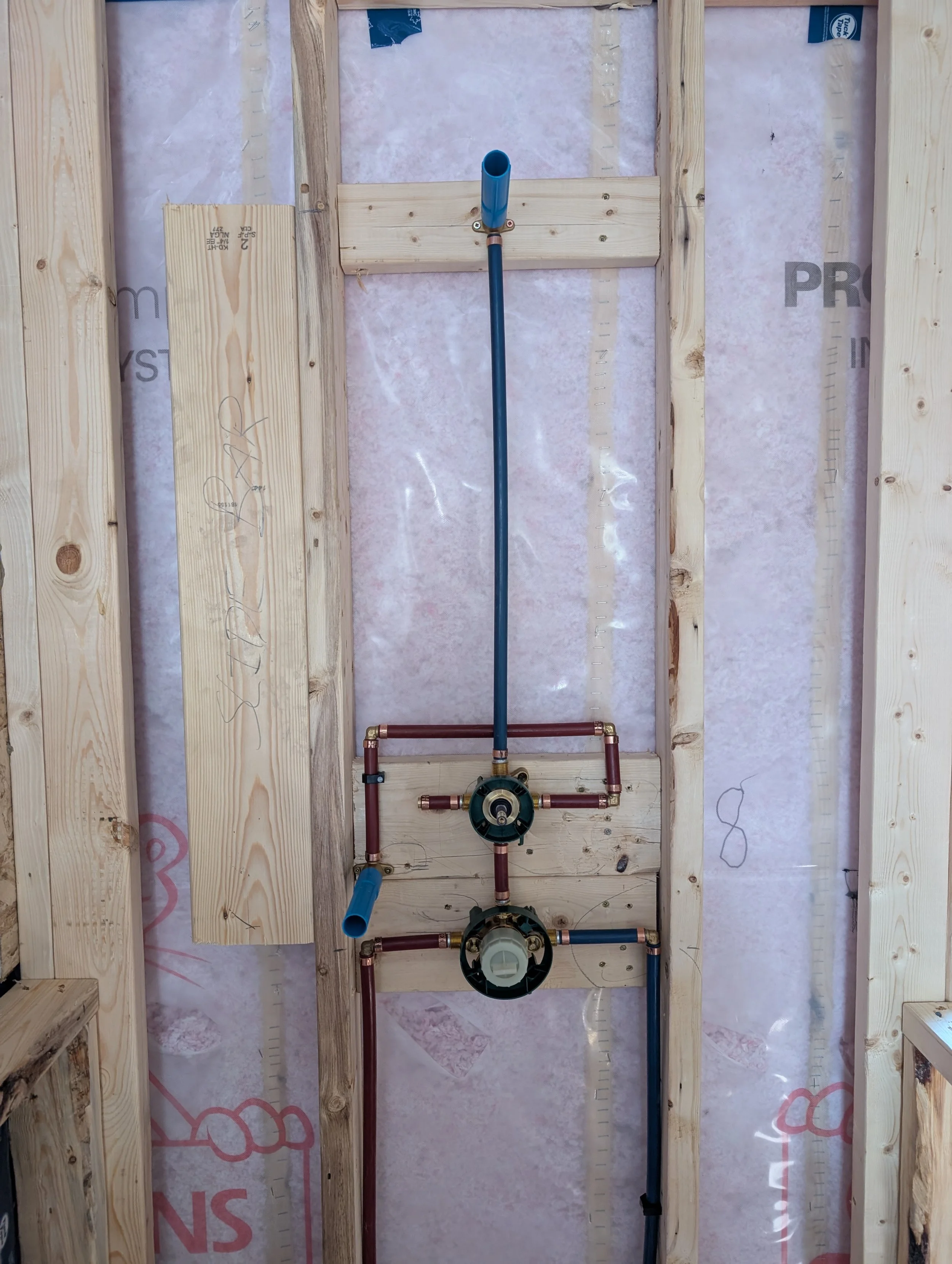 A plumbing system installed within a wooden wall frame, featuring water pipes, a pump, and fittings for a residential or commercial building.