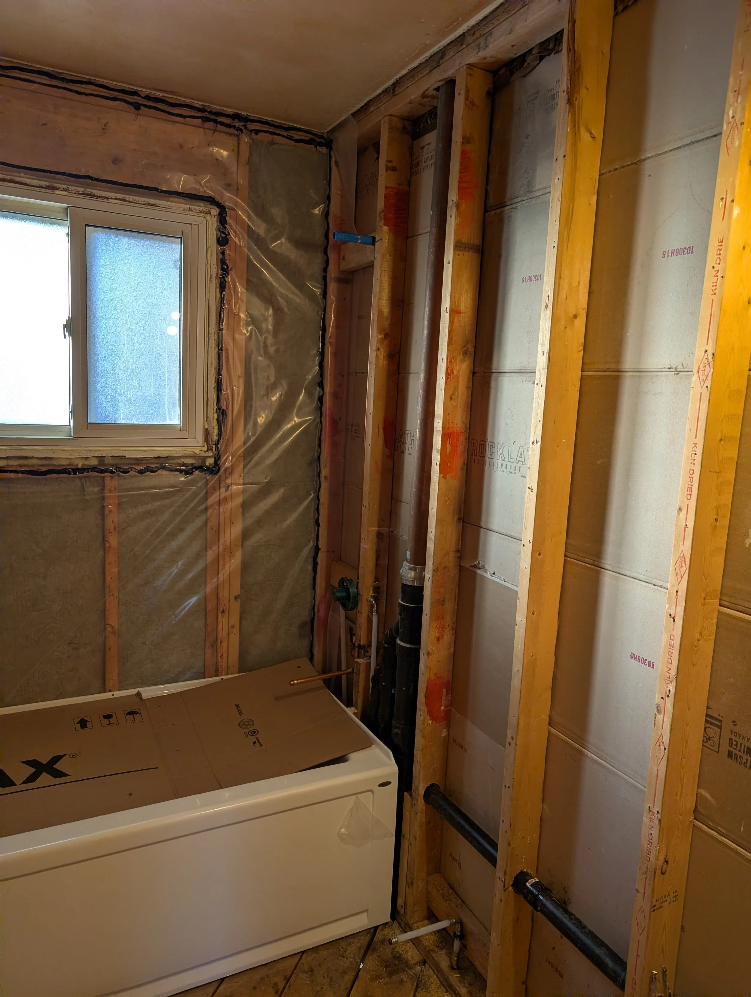 Bathroom under construction with pipes and unfinished wall framing.