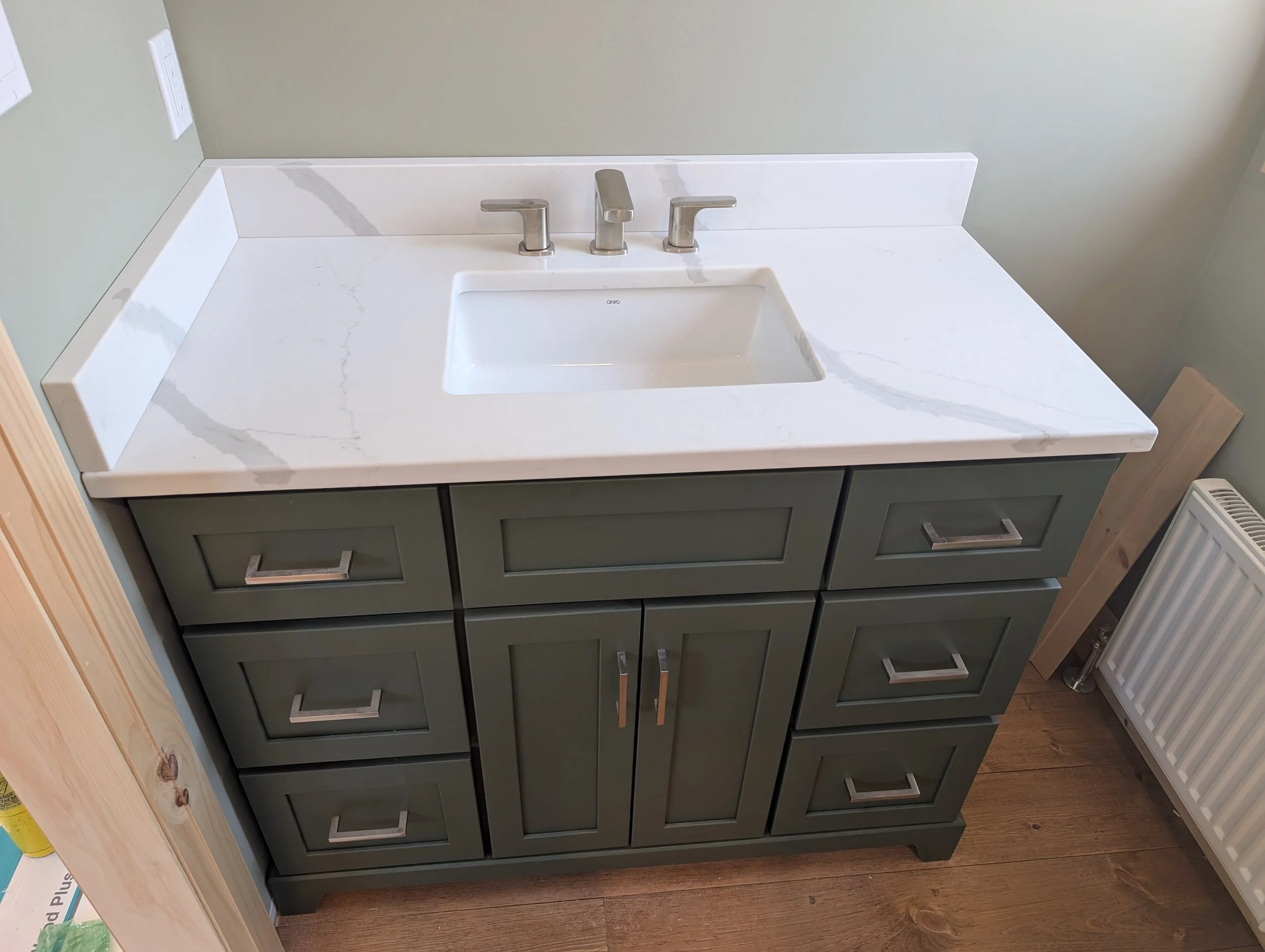 A bathroom vanity with a white countertop, integrated sink, and modern chrome faucet and handles. The cabinet below is painted dark gray with silver handles.