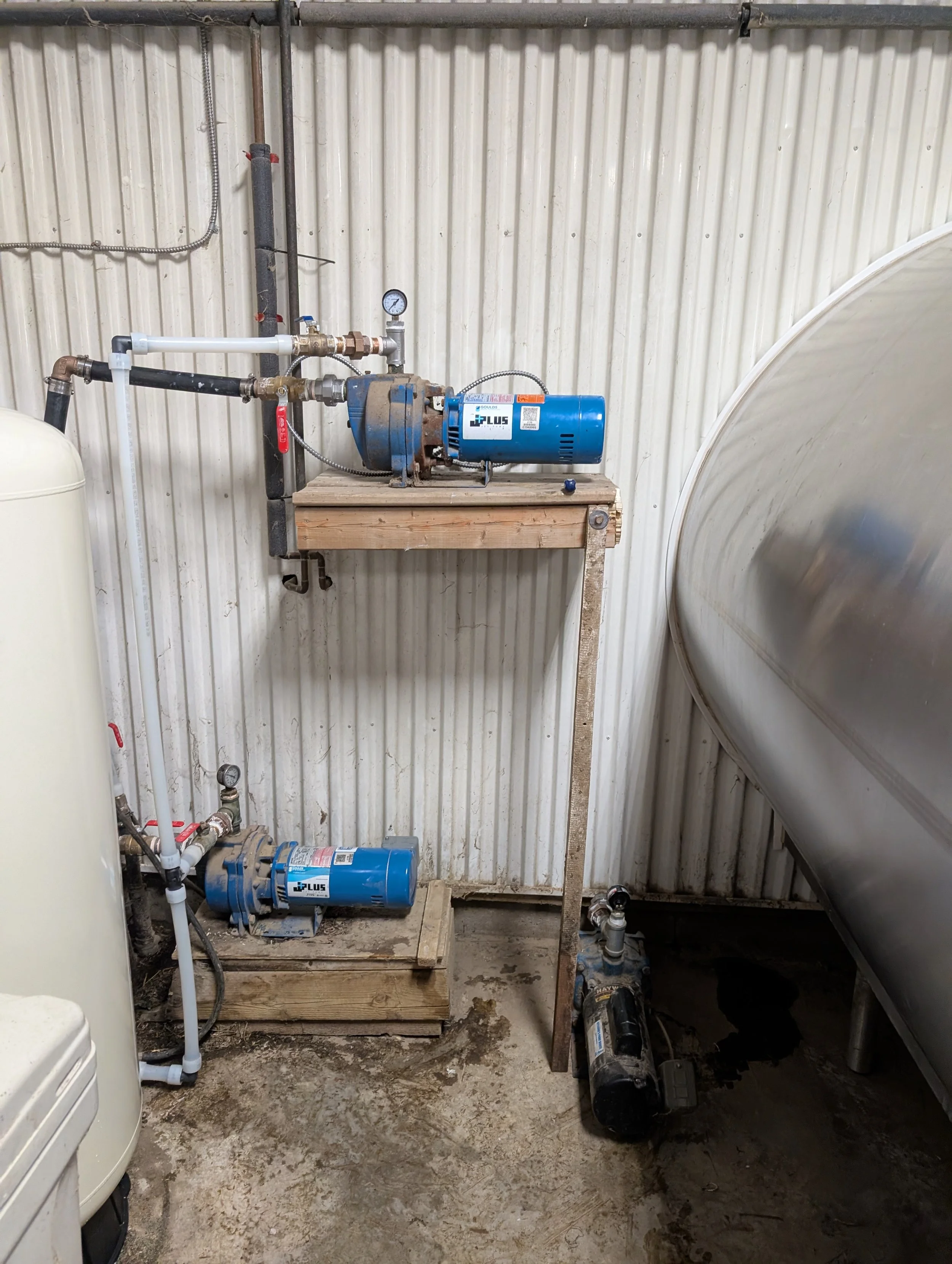 A pump system with pipes, gauges, and a motor installed on a wooden platform in a utility room with metal walls. The setup appears to be for water or fluid circulation or filtration.