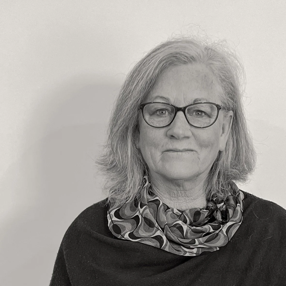 Black and white headshot of Veronica, looking at the camera and smiling, with shoulder-length light hair and glasses.