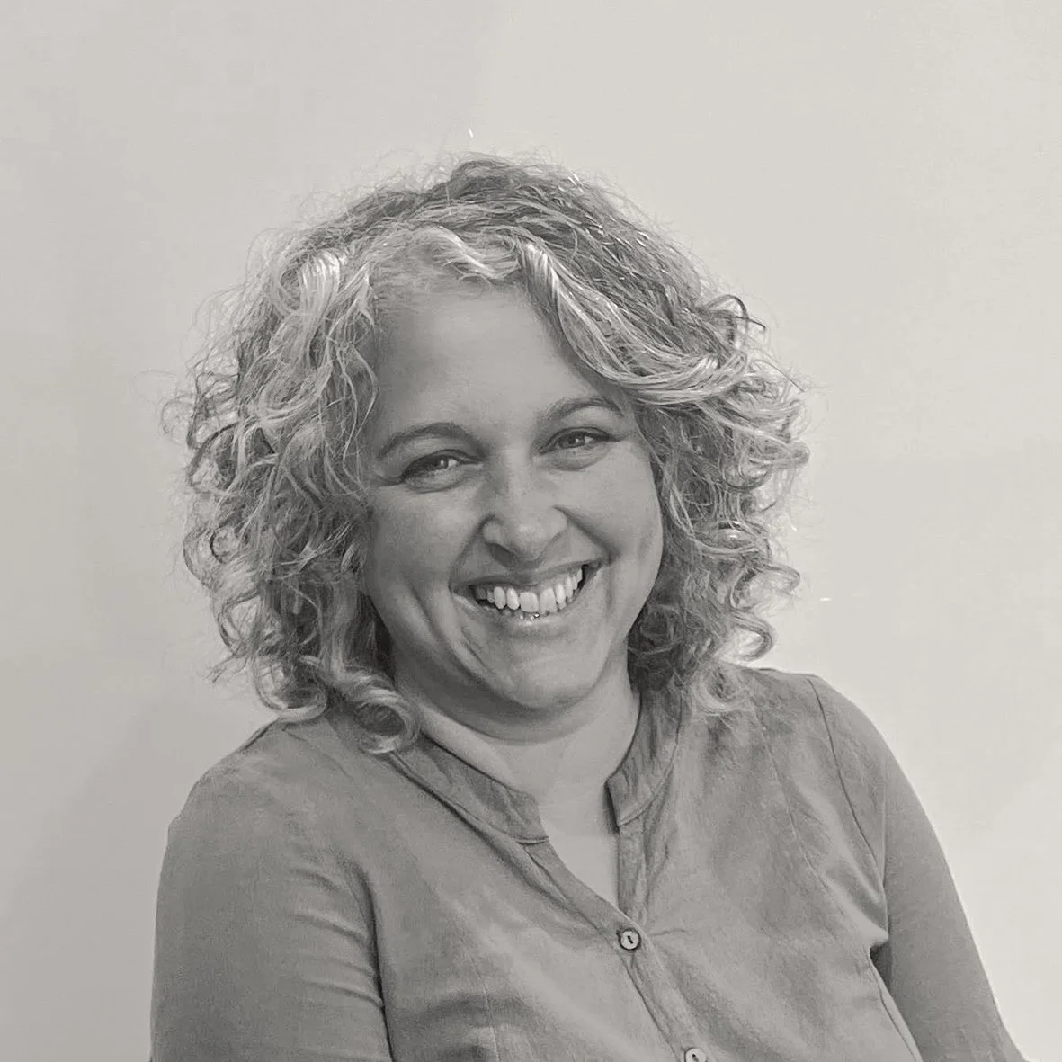 Black and white headshot of Mary, a smiling woman with curly brown hair.