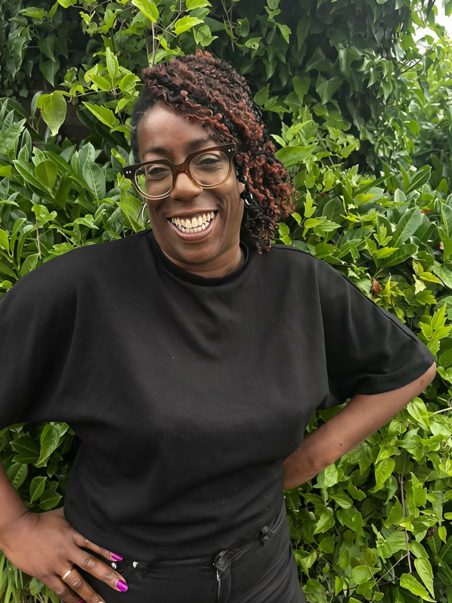 Headshot of Sharon, who has dark skin, wearing glasses and sporting a friendly smile.
