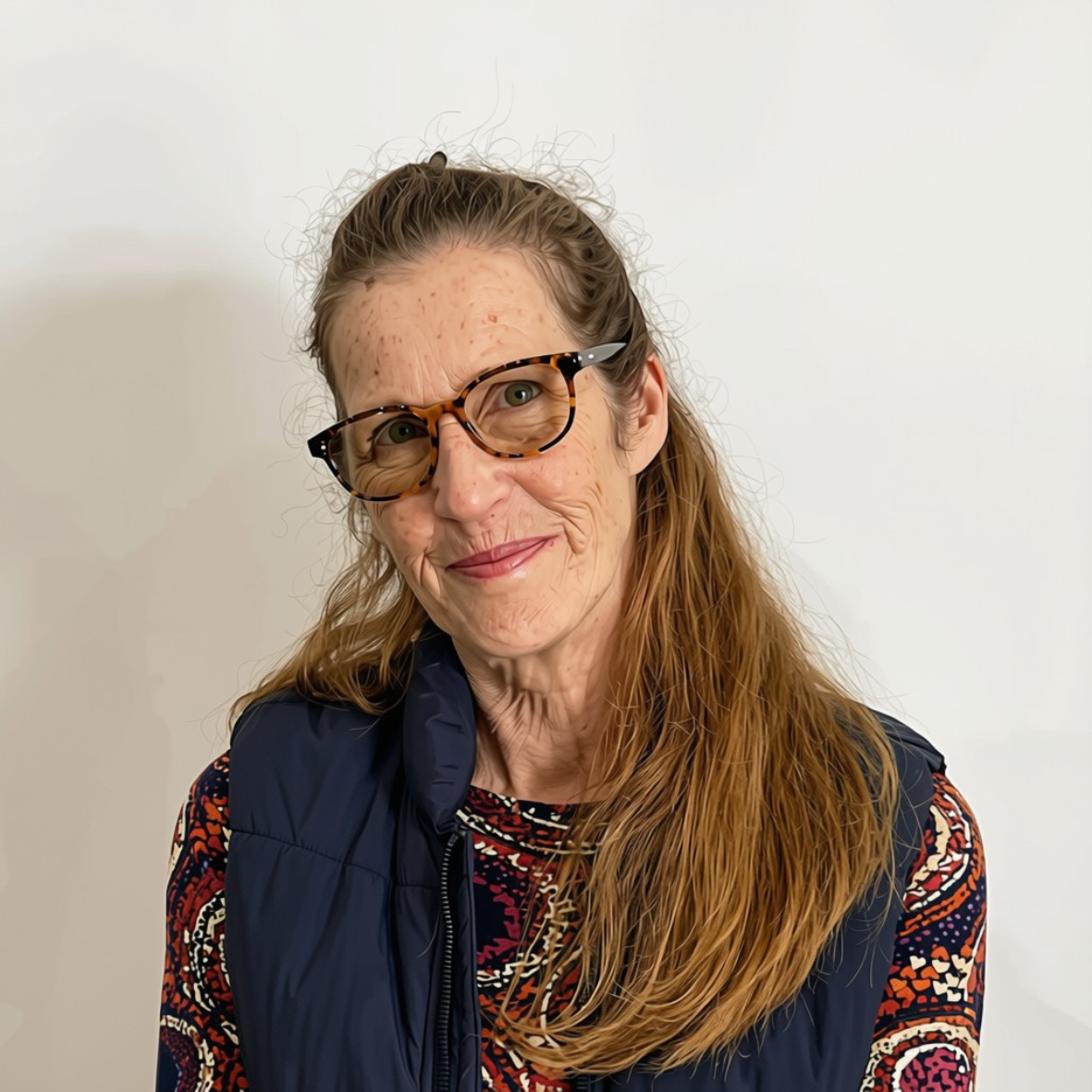 headshot of Polly, with half-up, half-down hair draped over one shoulder, smiling and wearing glasses.