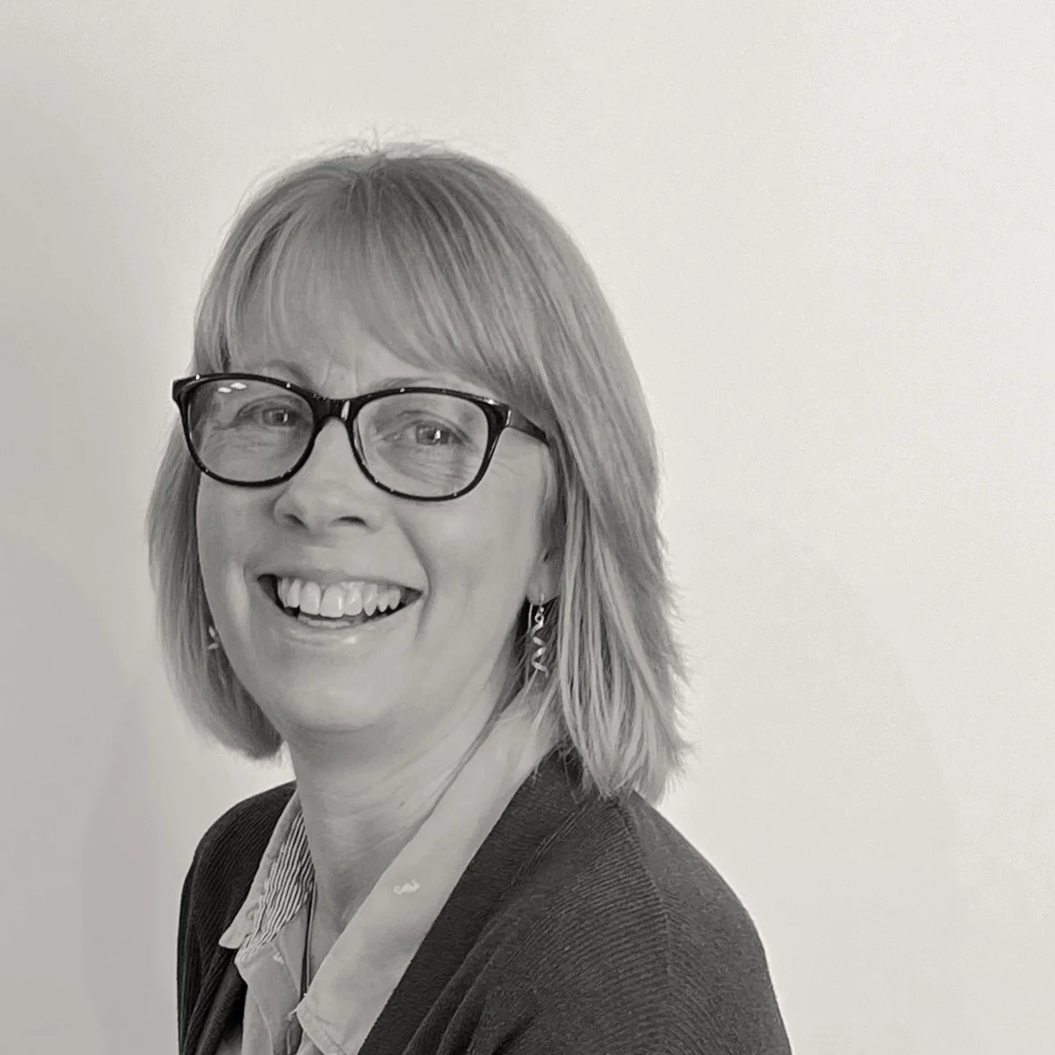 Black and white headshot of Sally who has a blonde bob wearing glasses smiling.
