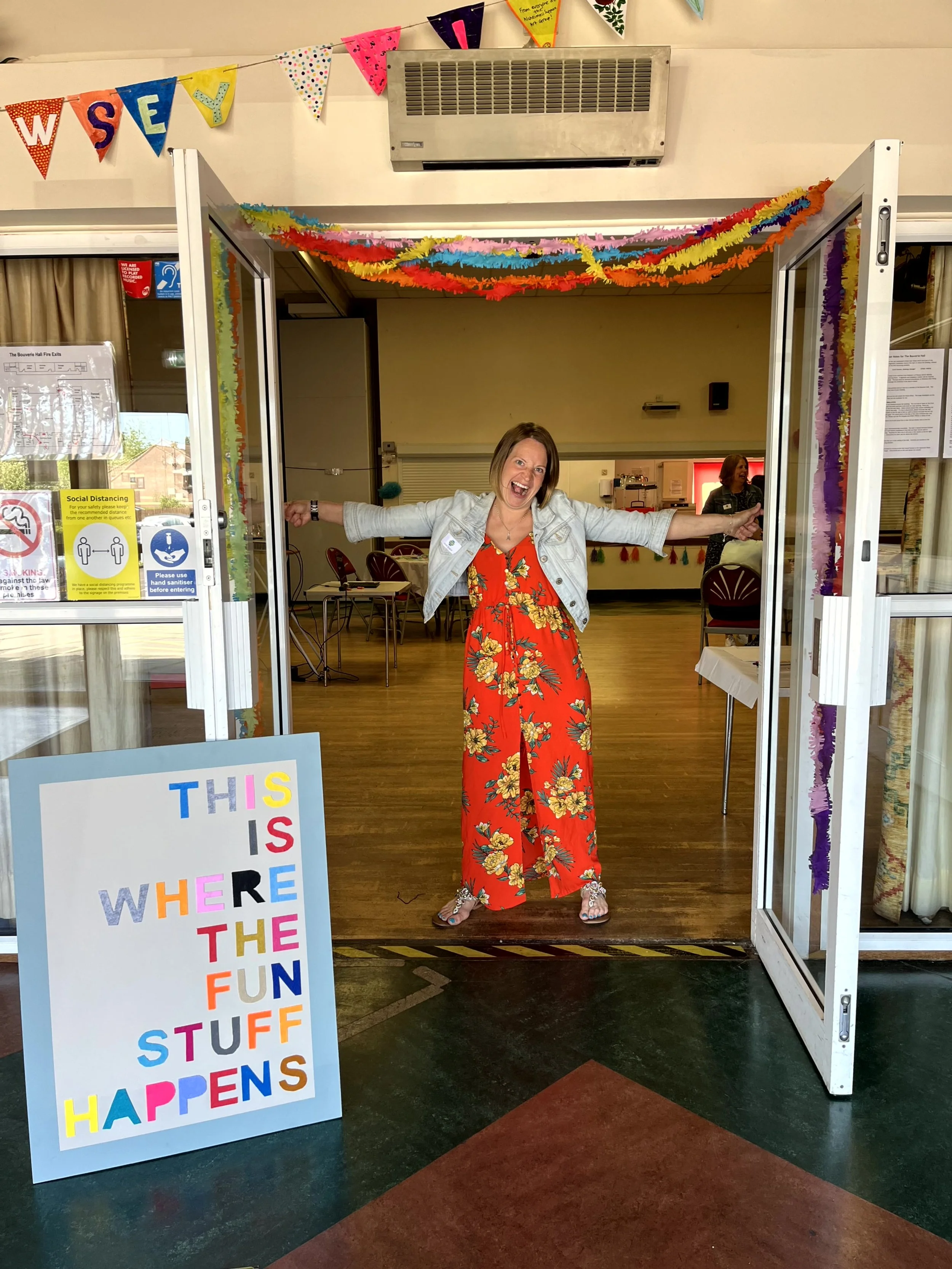 Abbie standing with arms wide open next to a sign which reads this is where the fun stuff happens
