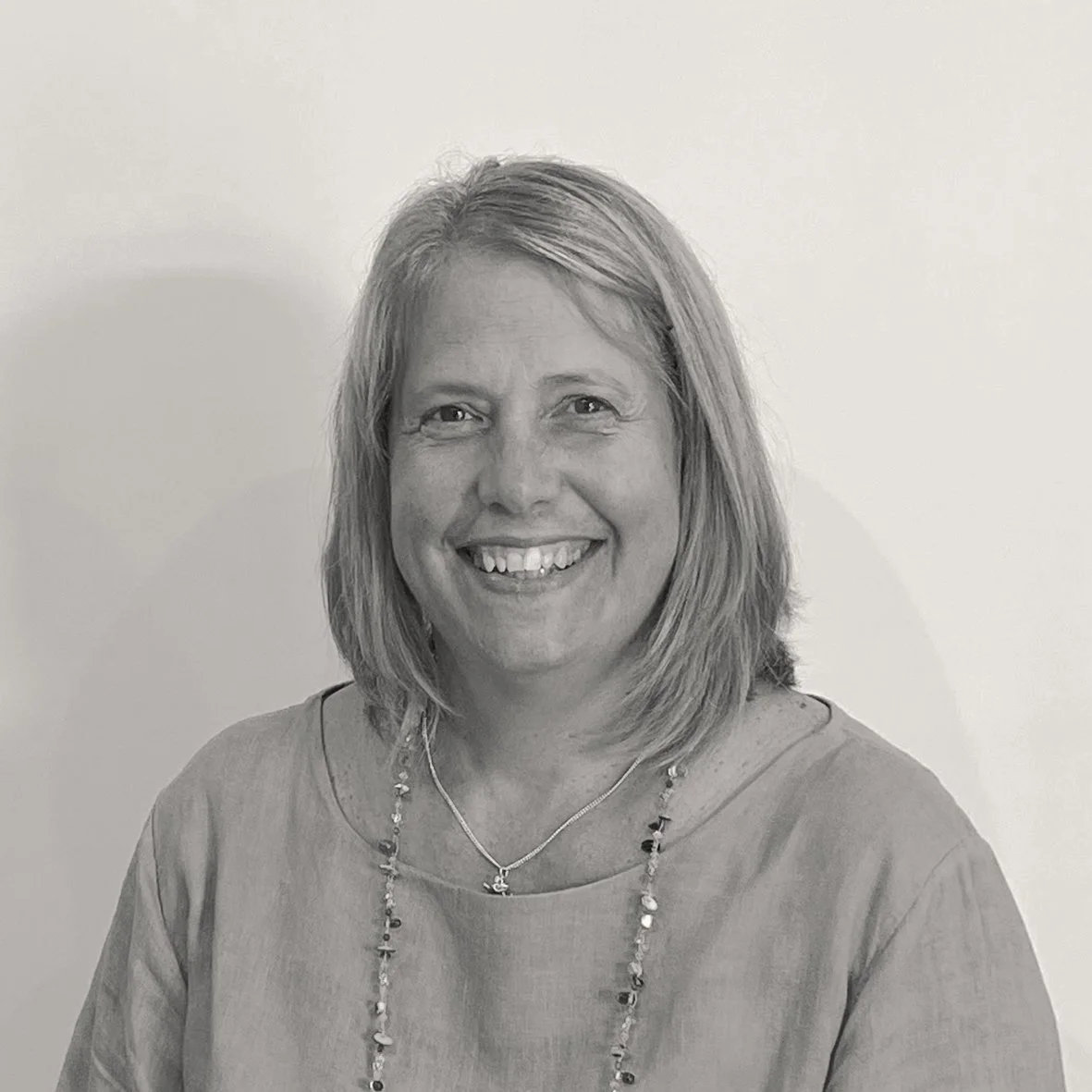 Black and white headshot of Katie, with chin-length light hair, smiling at the camera