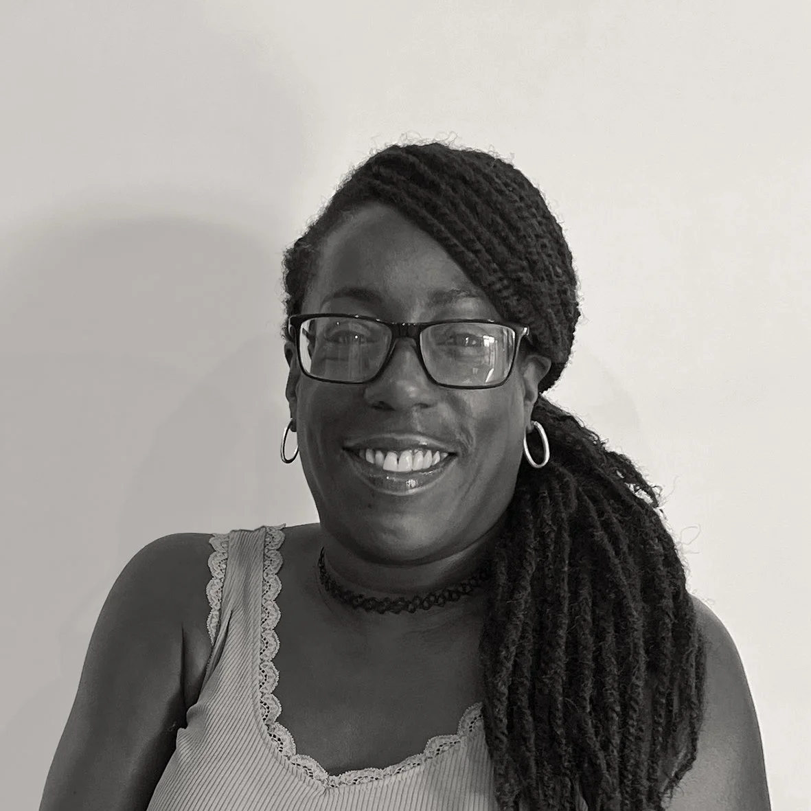 Black and white headshot of Sharon, who has dark skin, wearing glasses and sporting a friendly smile.