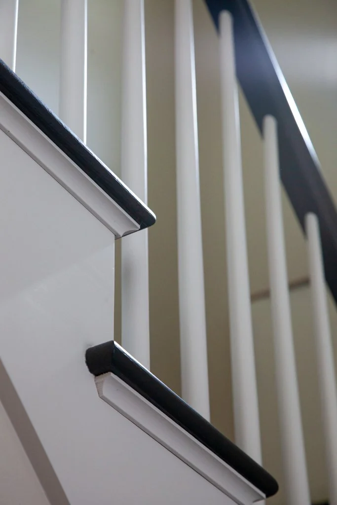 Close-up of a staircase with dark-colored handrails and white vertical balusters.