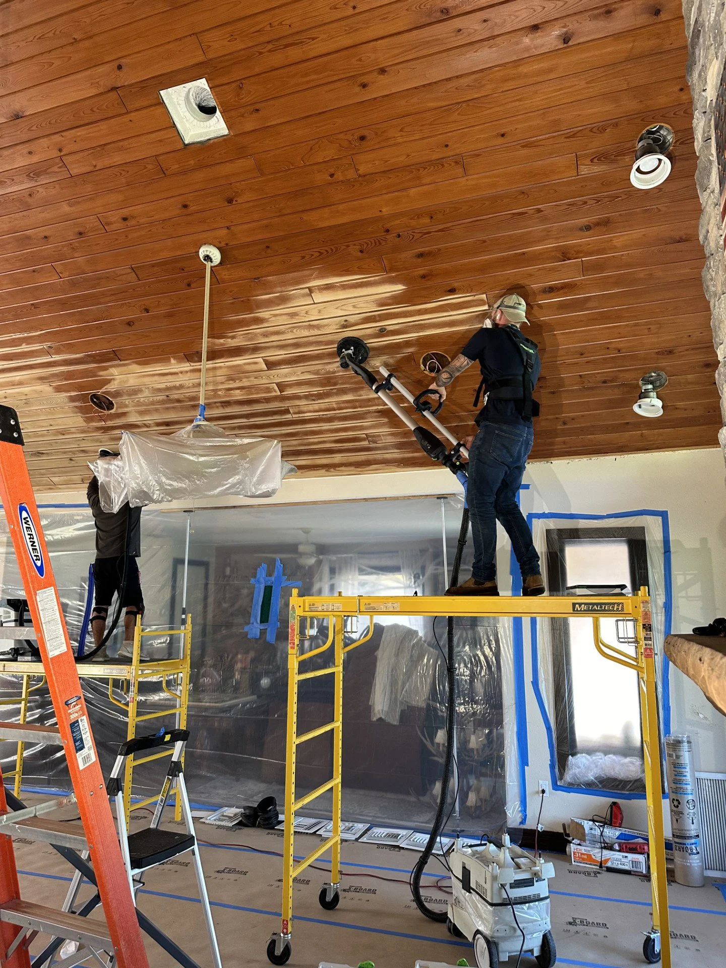 Workers installing a wood ceiling using scaffolding in a room under renovation.