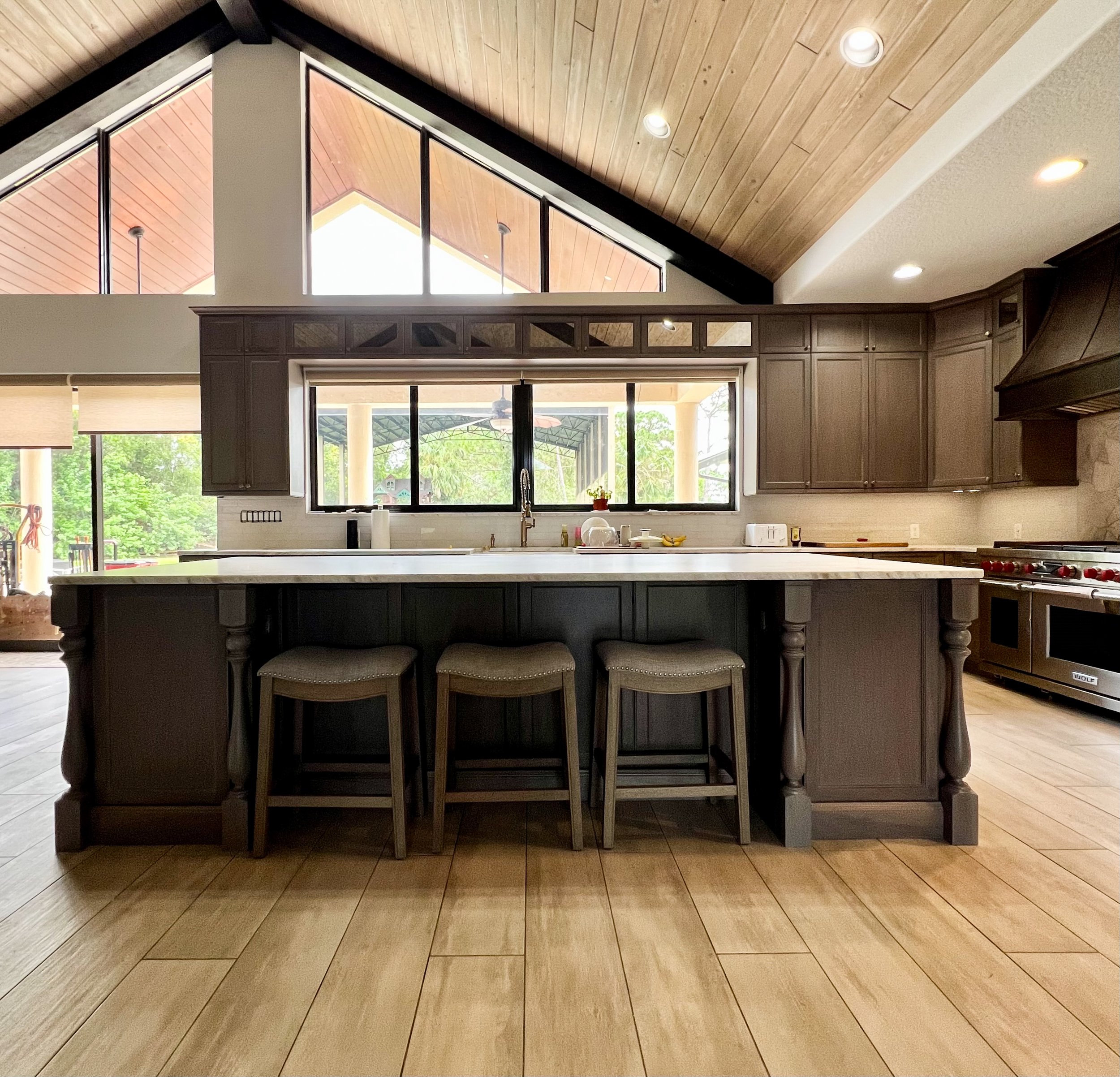 Modern kitchen with dark wood cabinets, a large island with seating, and a high vaulted ceiling with large windows and skylights.