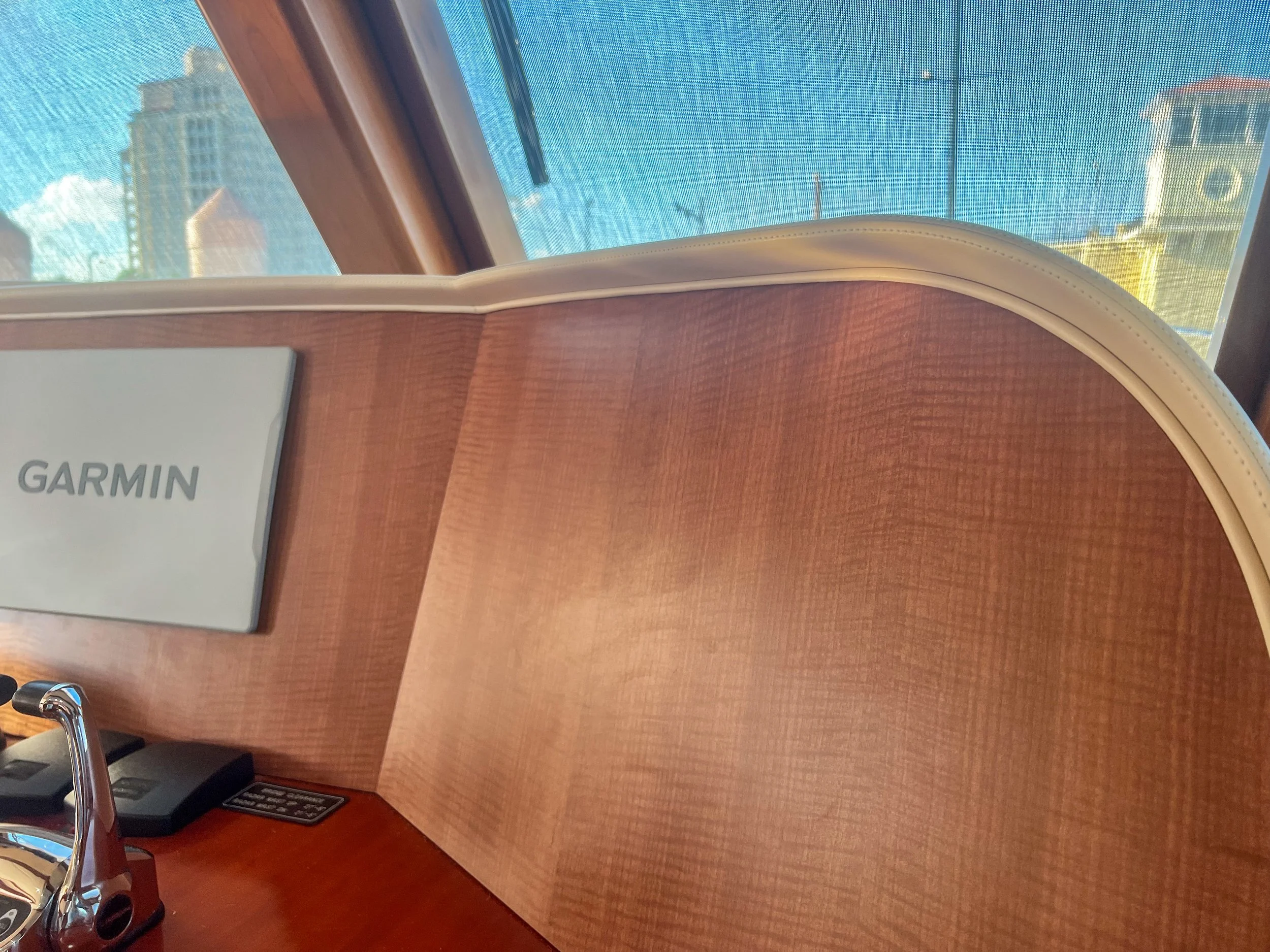 Close-up of a wooden desk with a Garmin sign, a microphone, and a phone, in front of a window with a cityscape view.