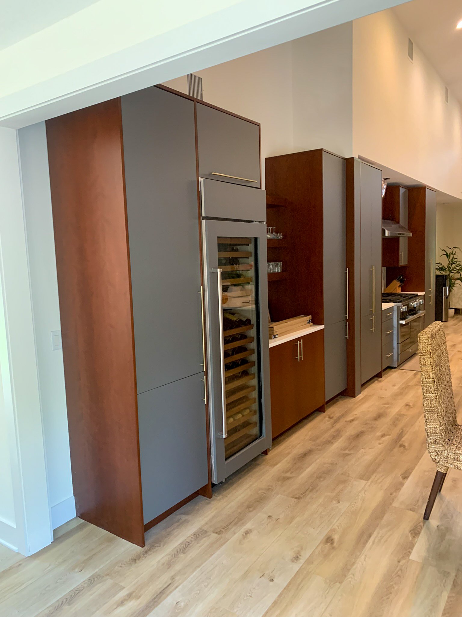 View of modern kitchen cabinetry, including a wine cooler, cabinets, and a gas stove with a range hood in an open floor plan with hardwood flooring.