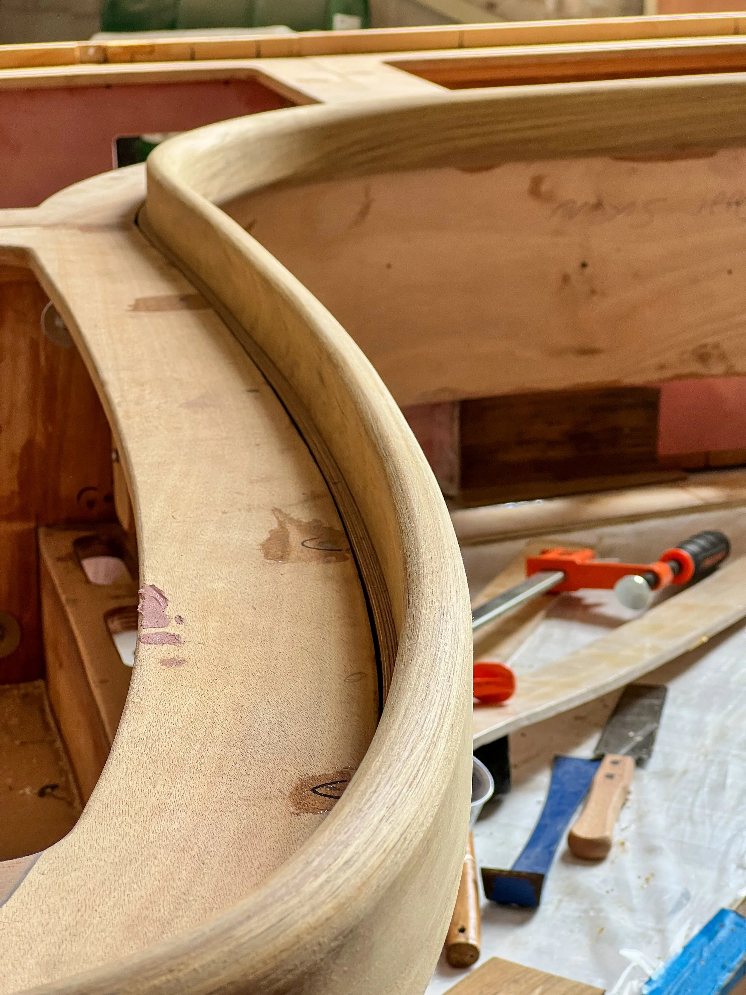 Close-up of a curved woodworking piece in a carpentry workshop with tools in the background.