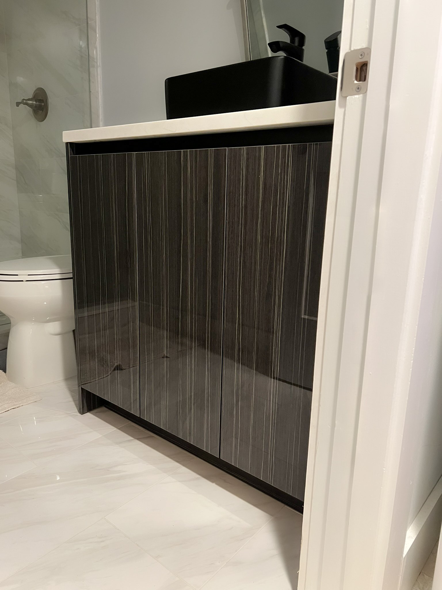 Bathroom with dark wood cabinet, black sink faucet, and white countertop, partially visible white toilet, and marble shower wall.