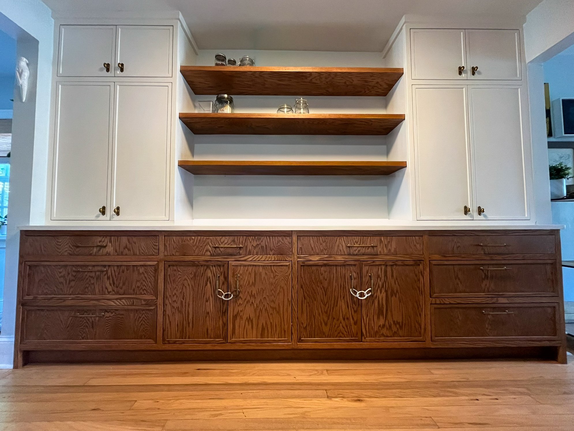 Built-in wooden cabinets with white upper doors and darker lower drawers, featuring open shelves in the middle with some jars on the upper shelves.
