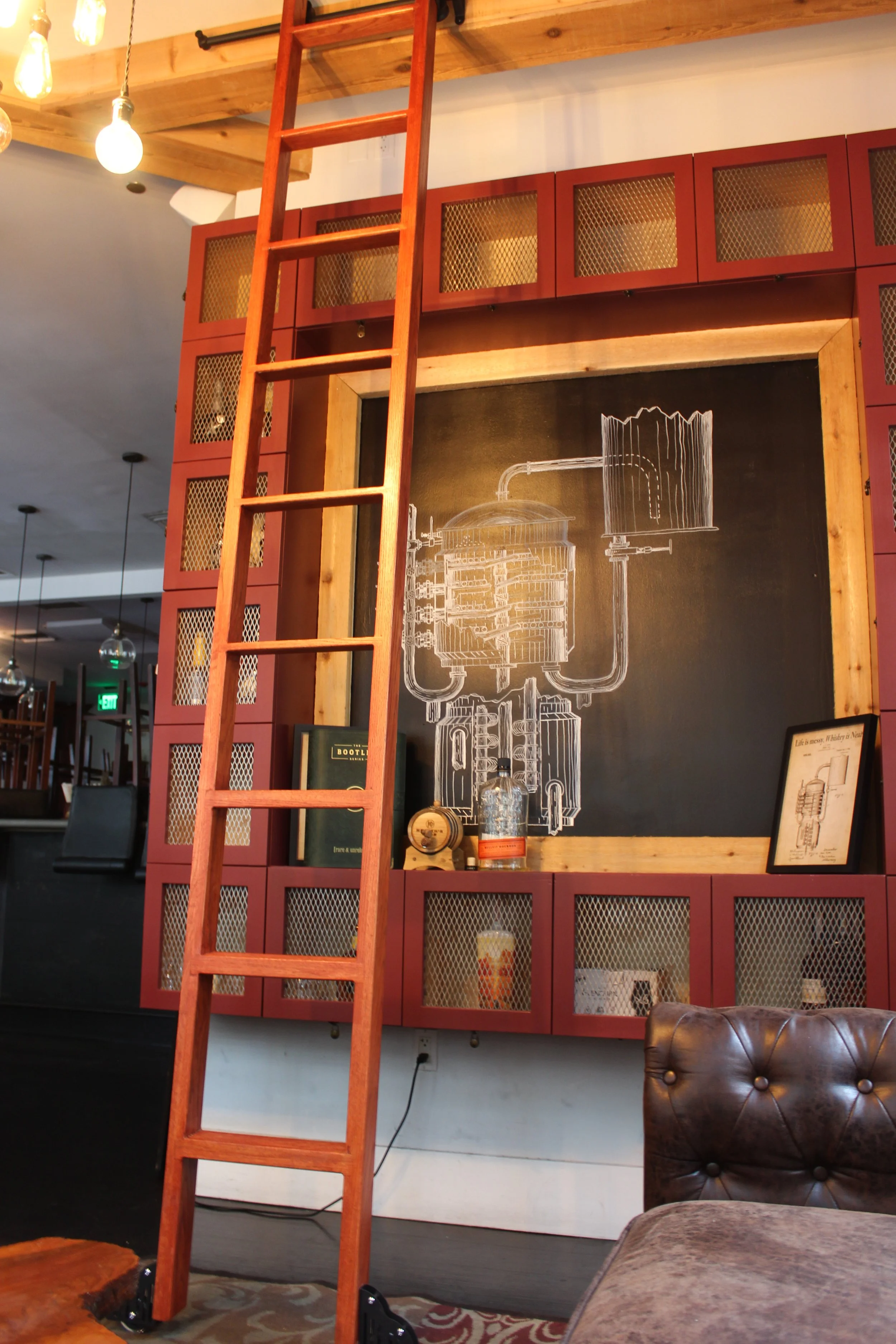 A wooden ladder leaning against a wall with red cabinetry and a chalkboard drawing of a distillation apparatus. There is seating and decor in the background of a cozy, industrial-style interior.