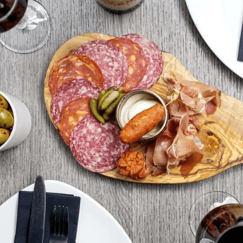 Charcuterie board with sliced meats, pickles, cheese, and dipping sauces on a wooden platter