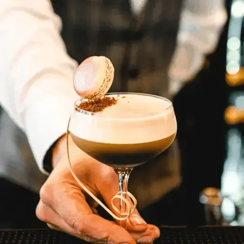 A person holding a cocktail glass with a marshmallow on the rim, whipped cream, coffee, and cocoa powder in the drink.