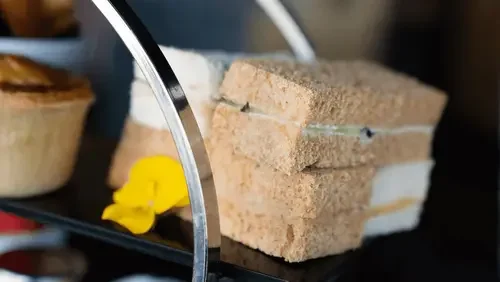 Stack of four sandwich halves with visible filling on a black tray, with a yellow flower in the background.
