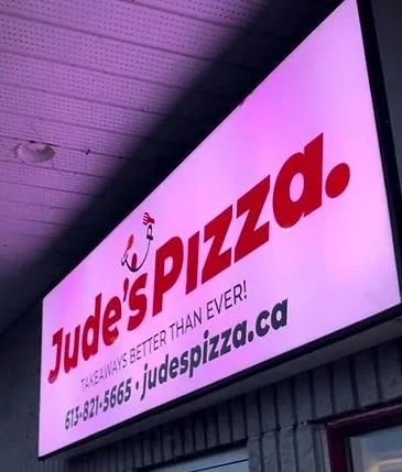 A sign for Jude's Pizza with contact information and website on the exterior of a building.