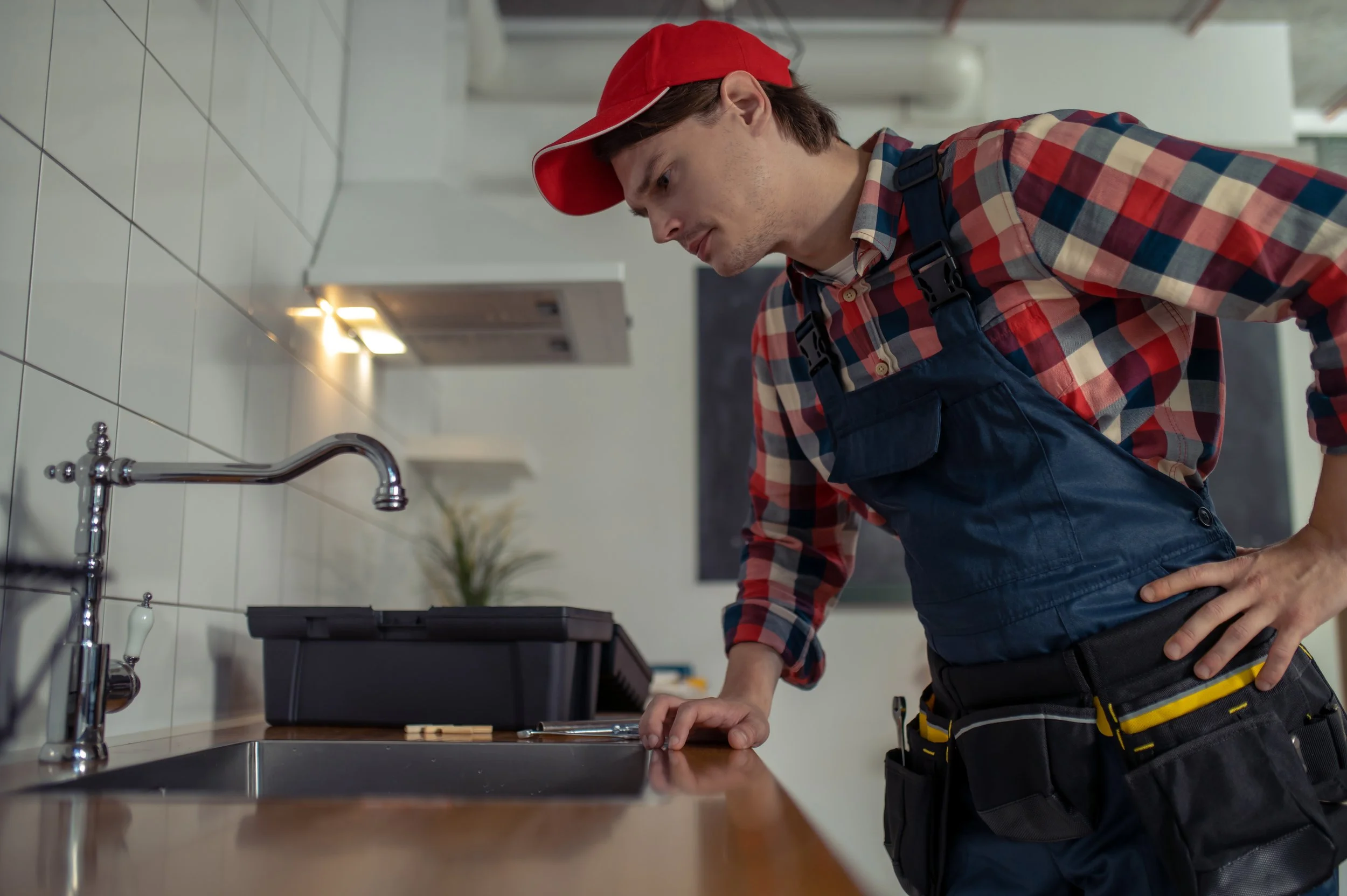 Plumber in red cap inspecting kitchen sink during water fixture retrofit service