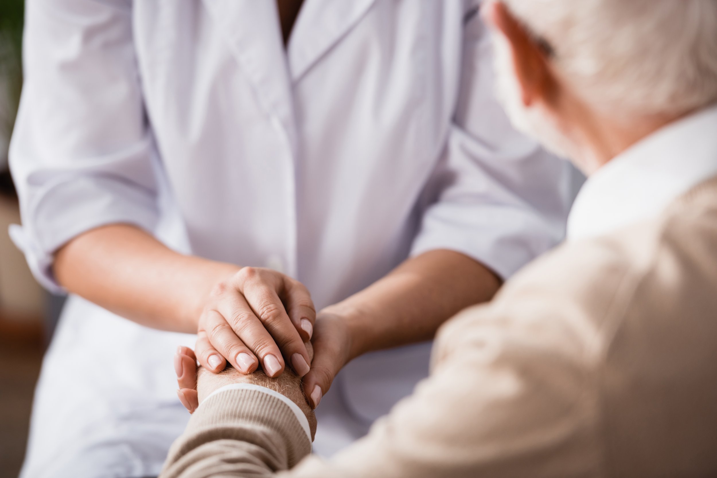 A person in a white shirt handshaking or holding hands with another person whose hand is visible, wearing a beige or light-colored long sleeve.