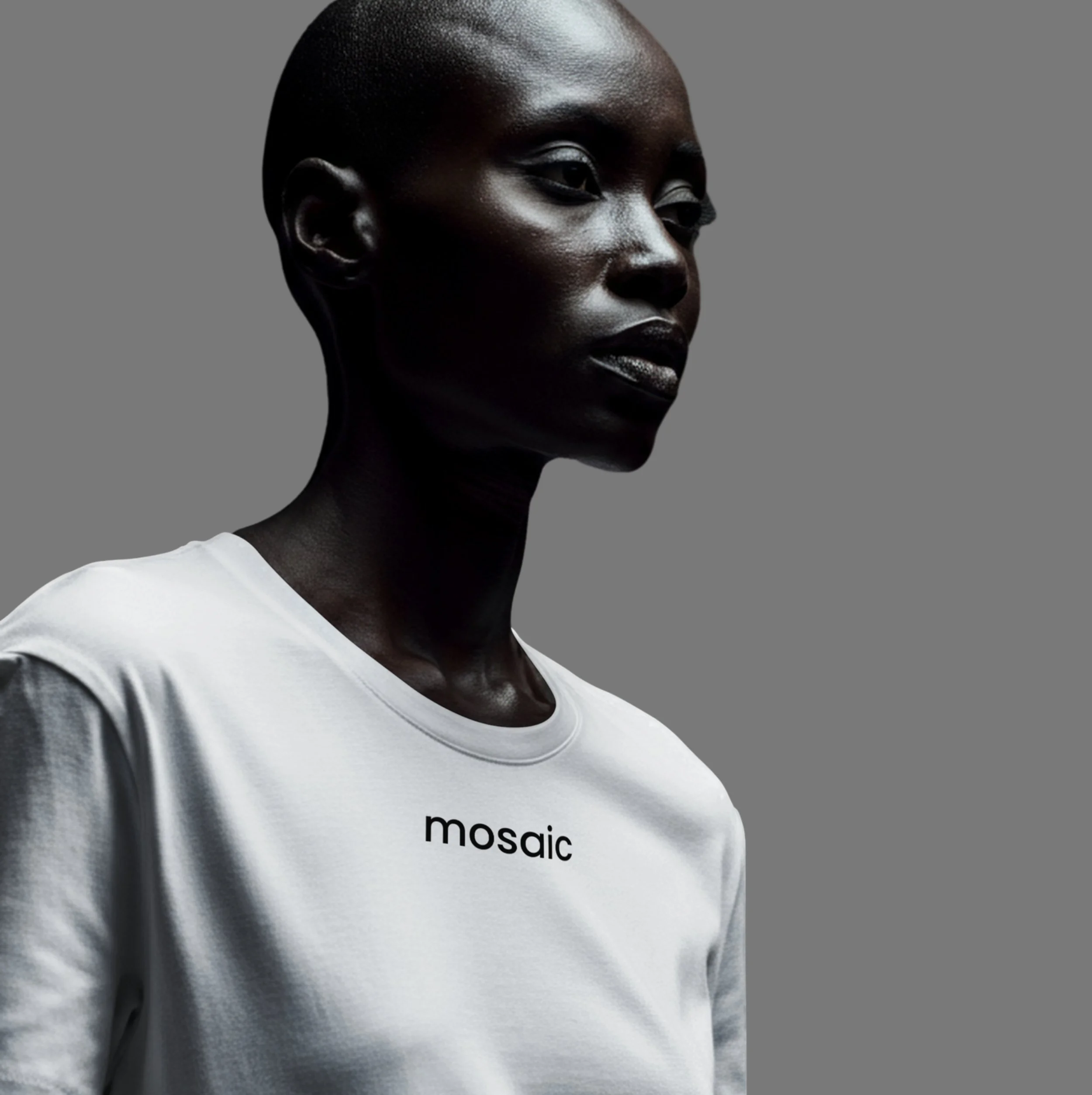 A woman with dark skin, short hair, wearing a white t-shirt with the word "mosaic" on it, standing against a plain gray background.