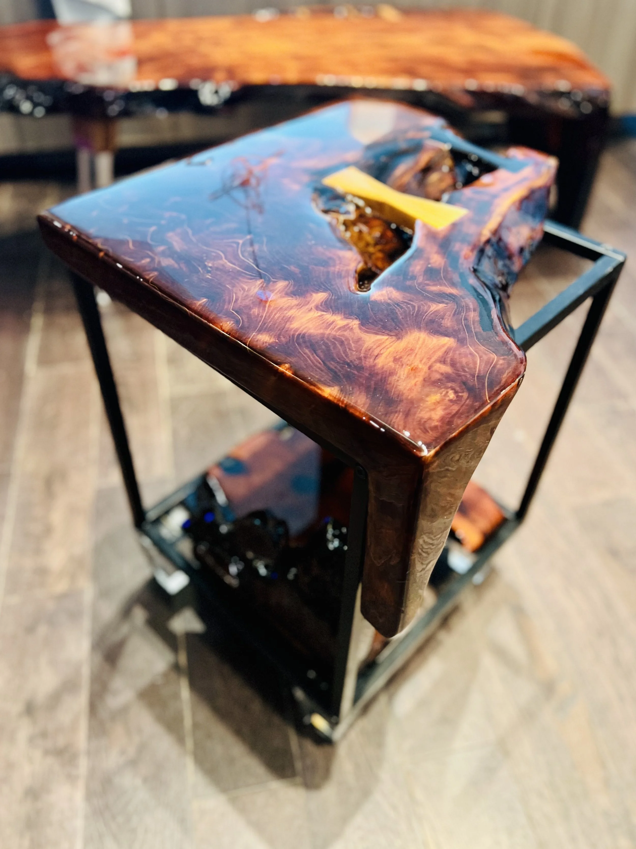 A small wooden table with a polished surface and a metal frame, with a decorative wooden design on top, set on a wooden floor.